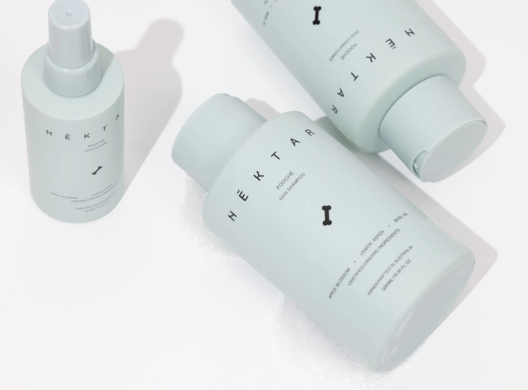 Three light blue bottles of dog care products, including shampoo and conditioner, with black text and small black bone icons, on a white surface.