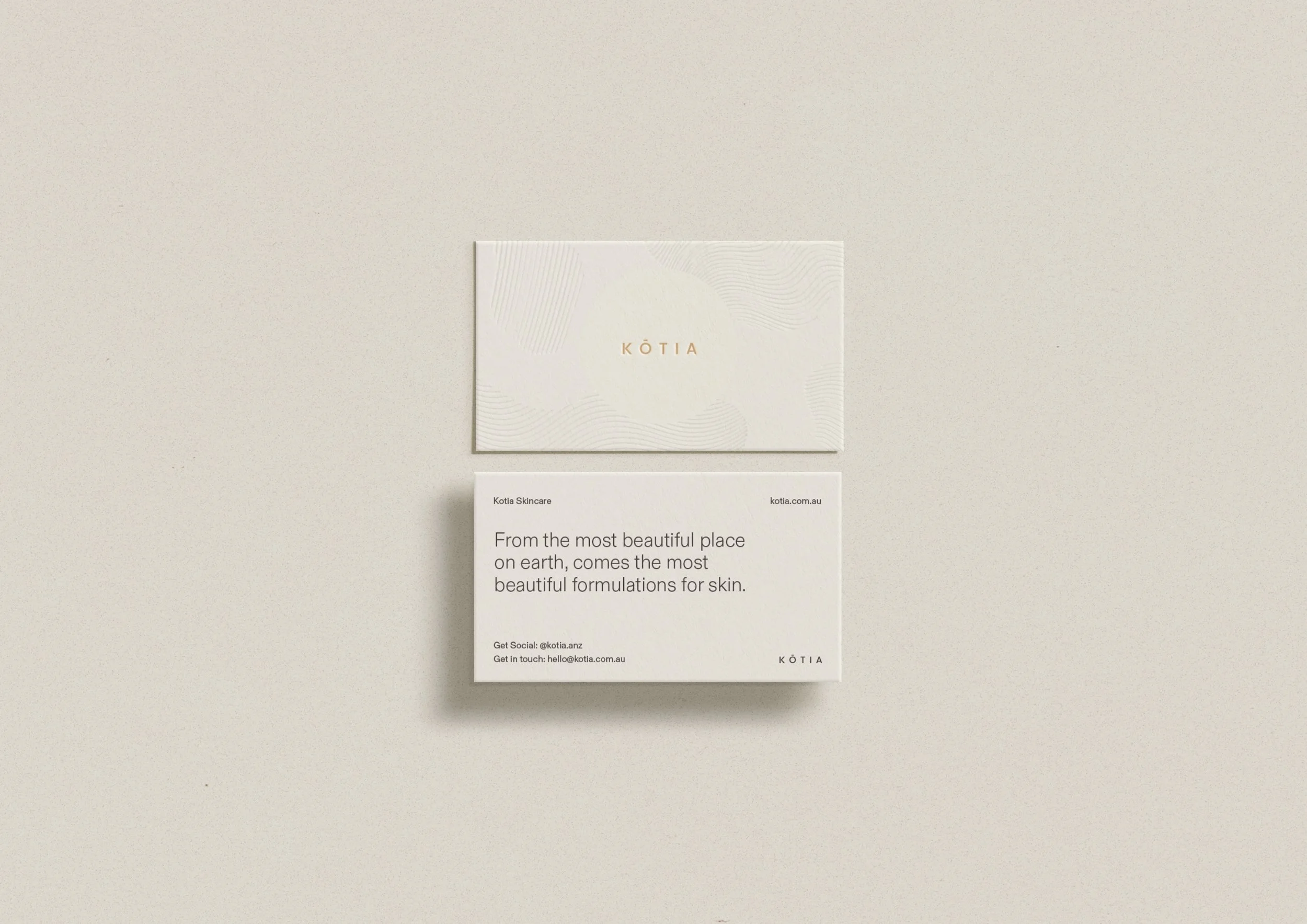 A beige business card with the brand name 'Kōtia' in gold lettering, and a white card with black text promoting skincare formulations, on a light neutral background.