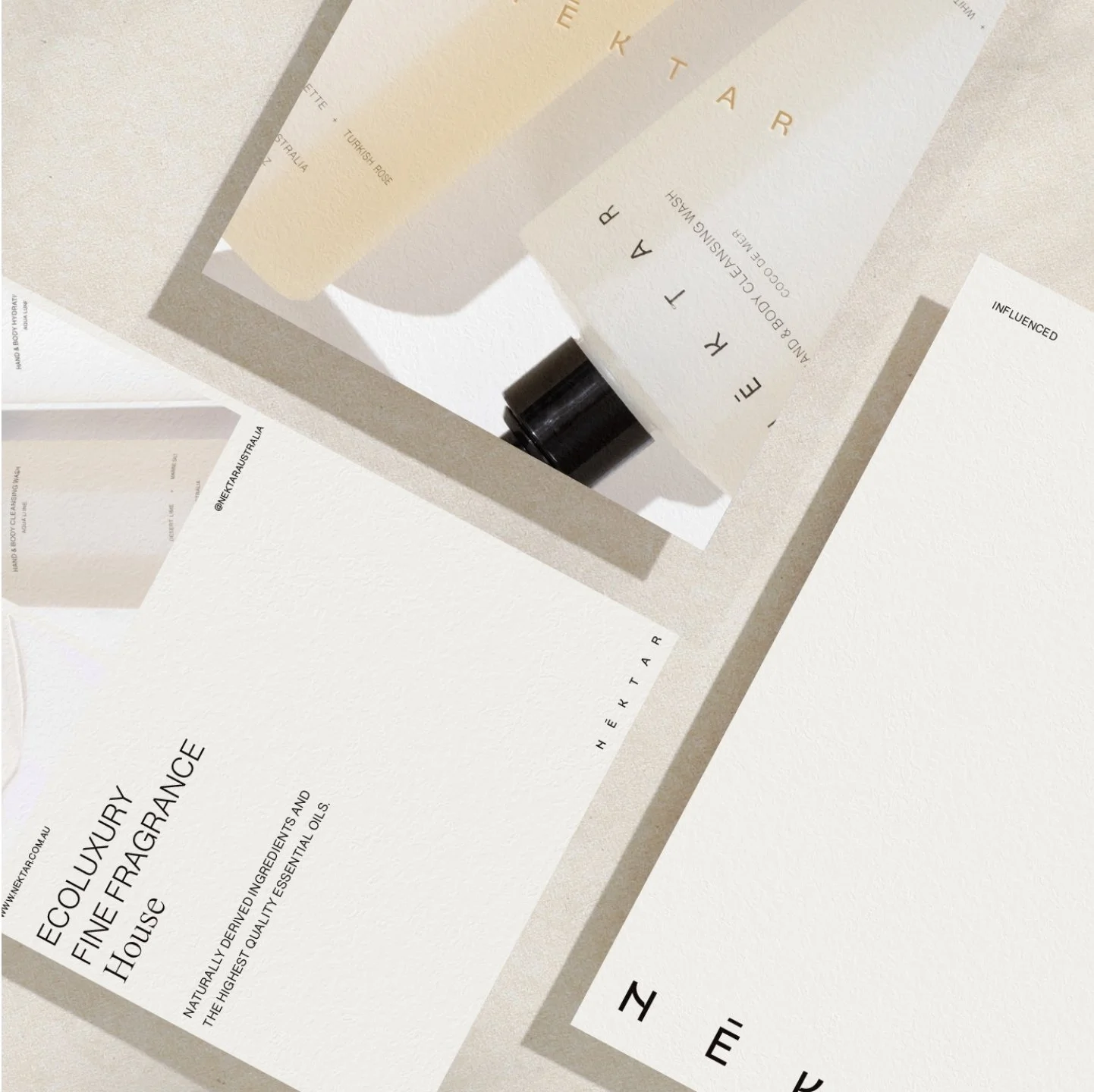 Several paper products including a white card, a beige card, and a brochure for eco-luxury fragrances, along with a small black vial, arranged on a white textured surface.
