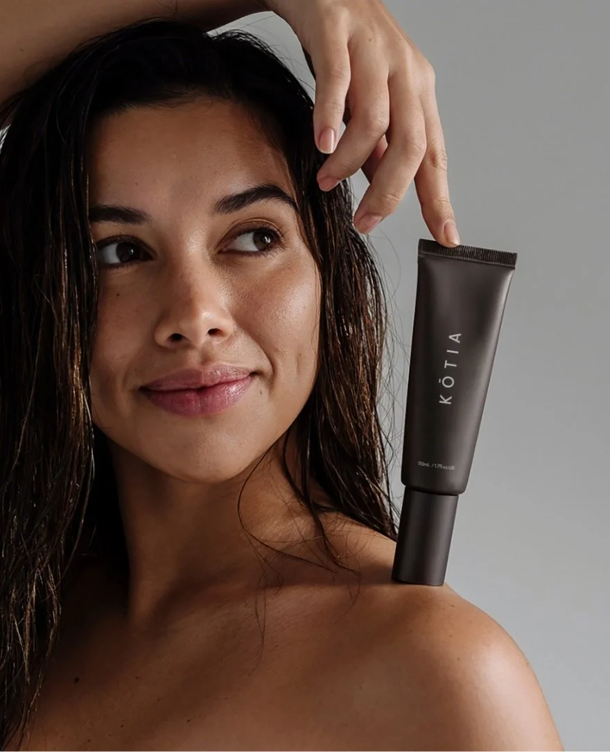 A woman with wet hair holding a KÖTI skincare tube on her shoulder.