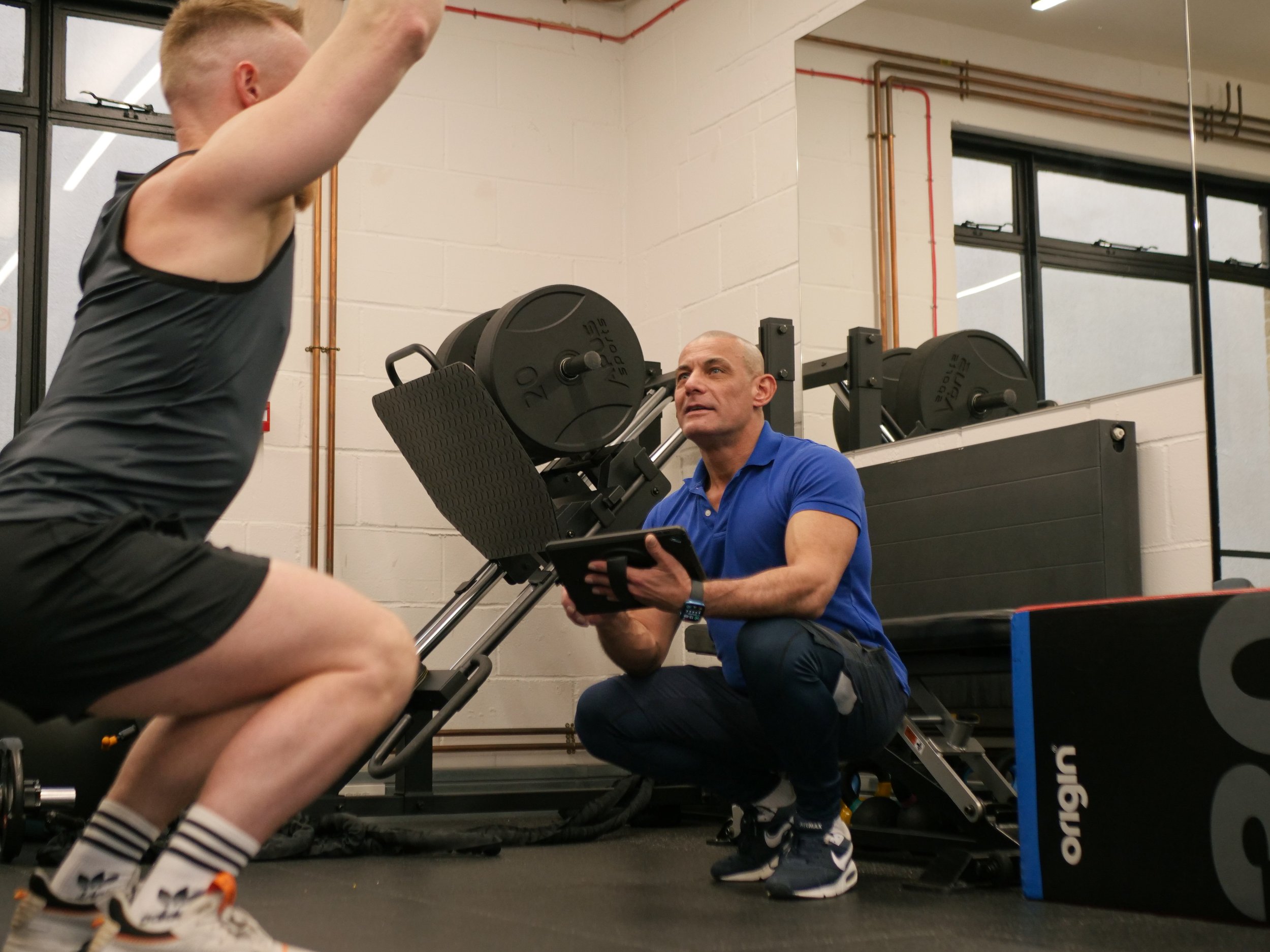 Personal trainer assessing a beginner’s overhead squat during a taster session at a private studio in Islington
