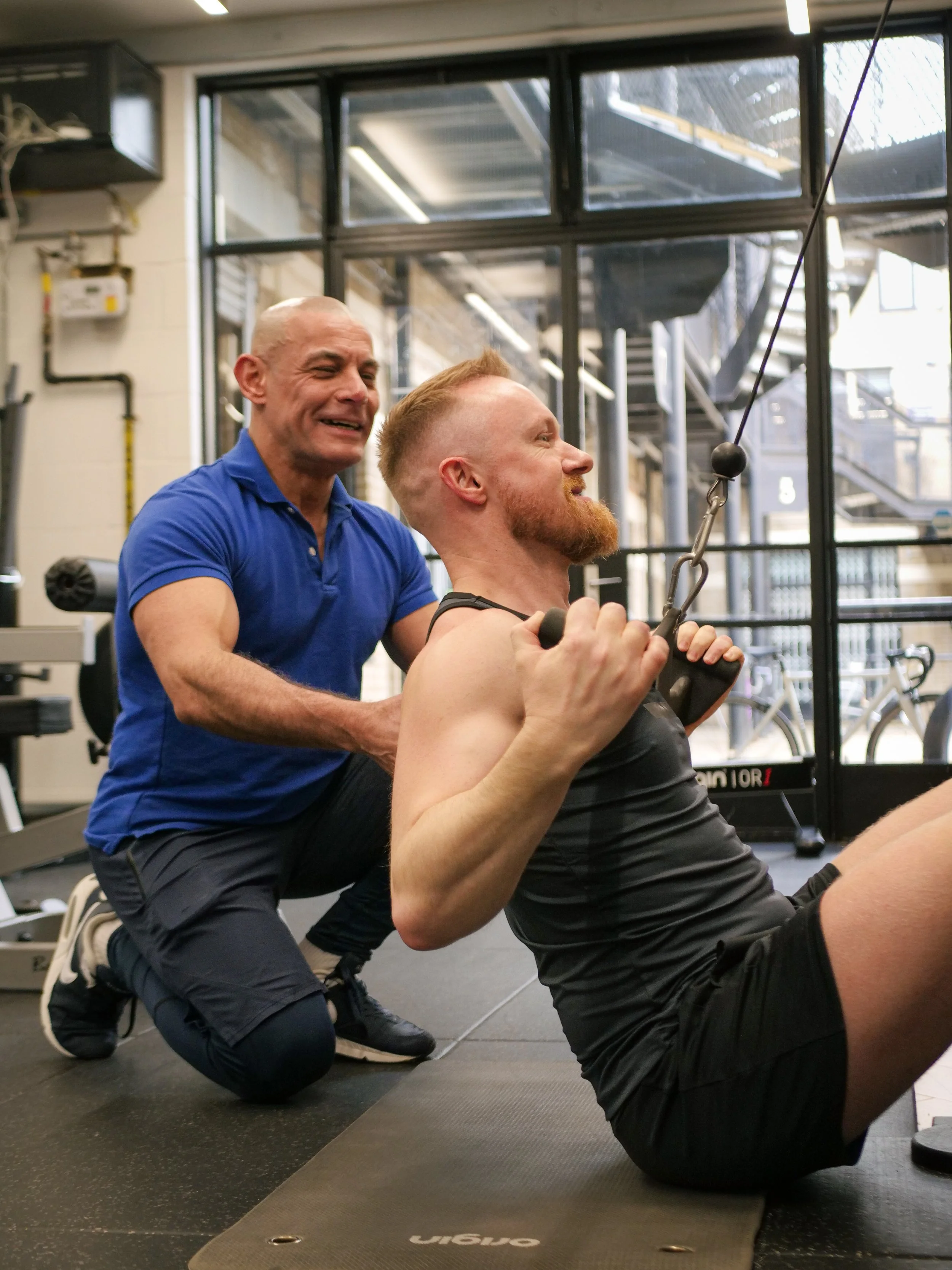 Male Personal Trainer in a private gym helping fit man doing lats pull down and strength training
