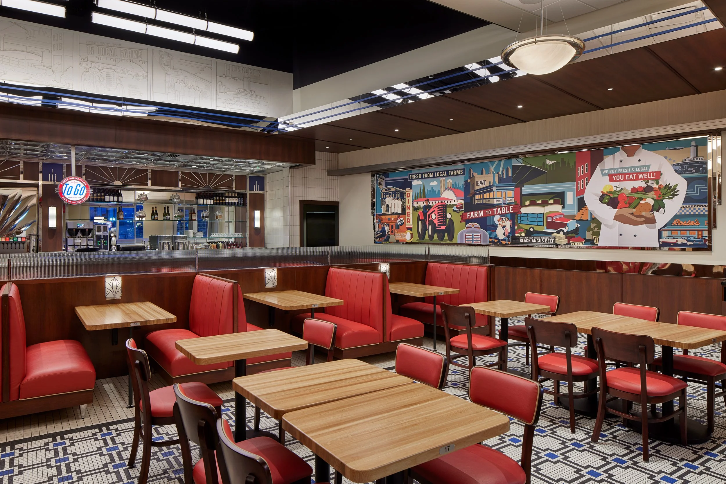 Empty restaurant dining area with red booth seating, wooden tables, and a colorful mural on the wall featuring farm-to-table themes.