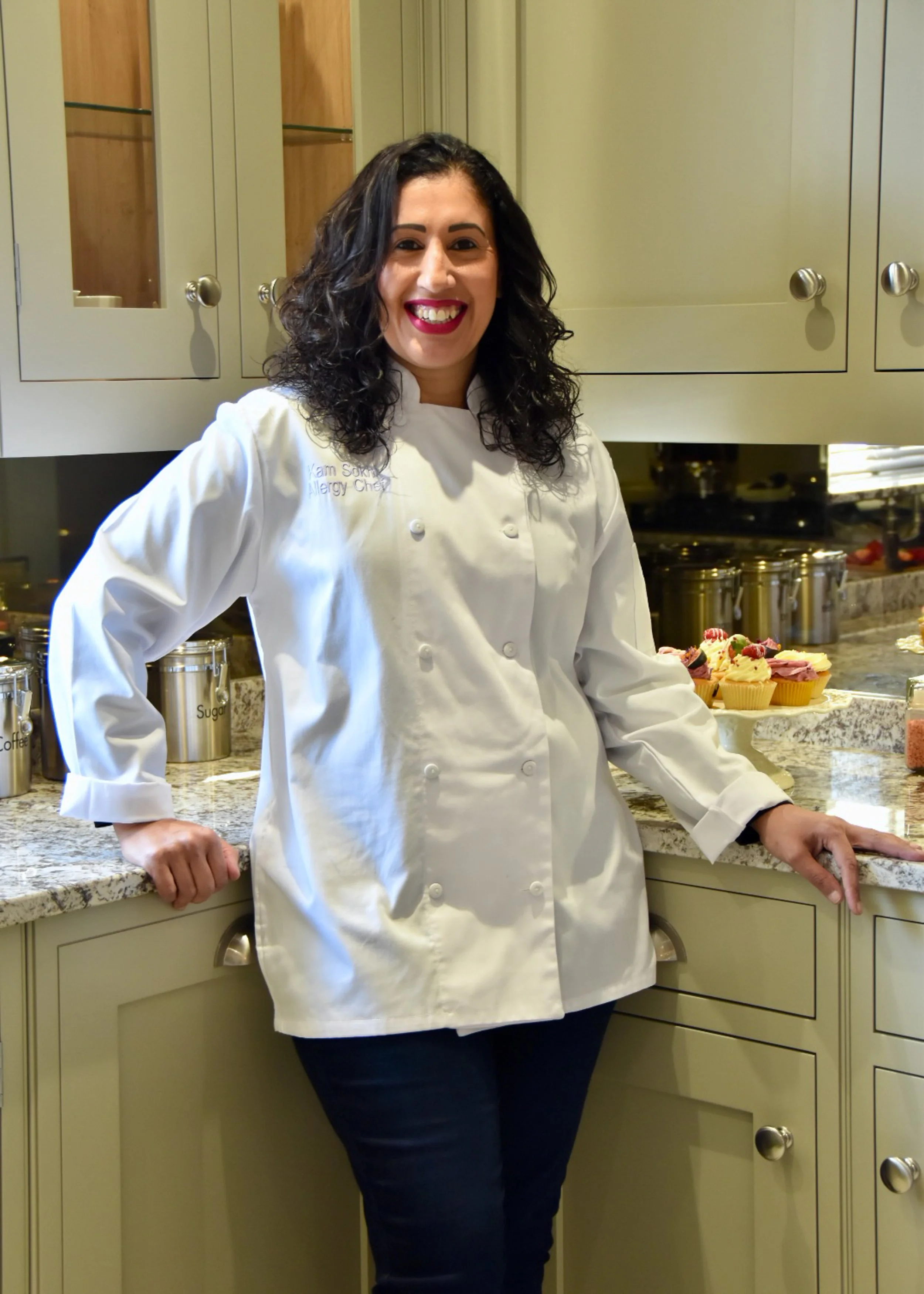 A picture of myself with chef whites in a beautiful kitchen with cupcakes in the background