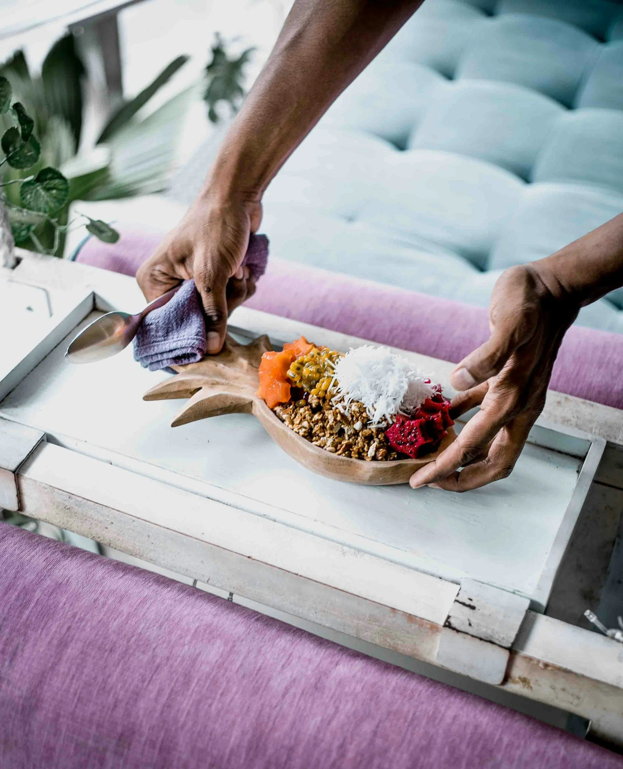 Person placing a tropical fruit and granola bowl on a white tray.