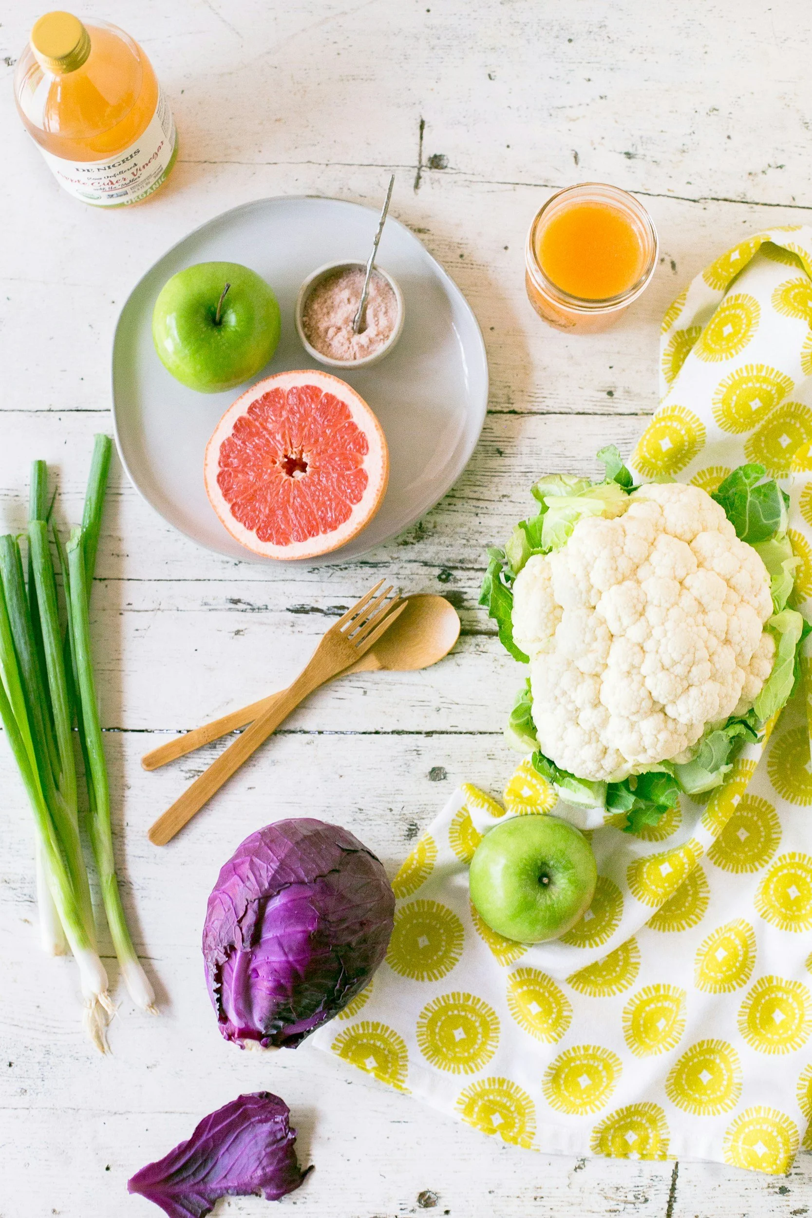 A picture of cauliflower, red cabbage on a table with a white plate with half a grapefruit and apple on it