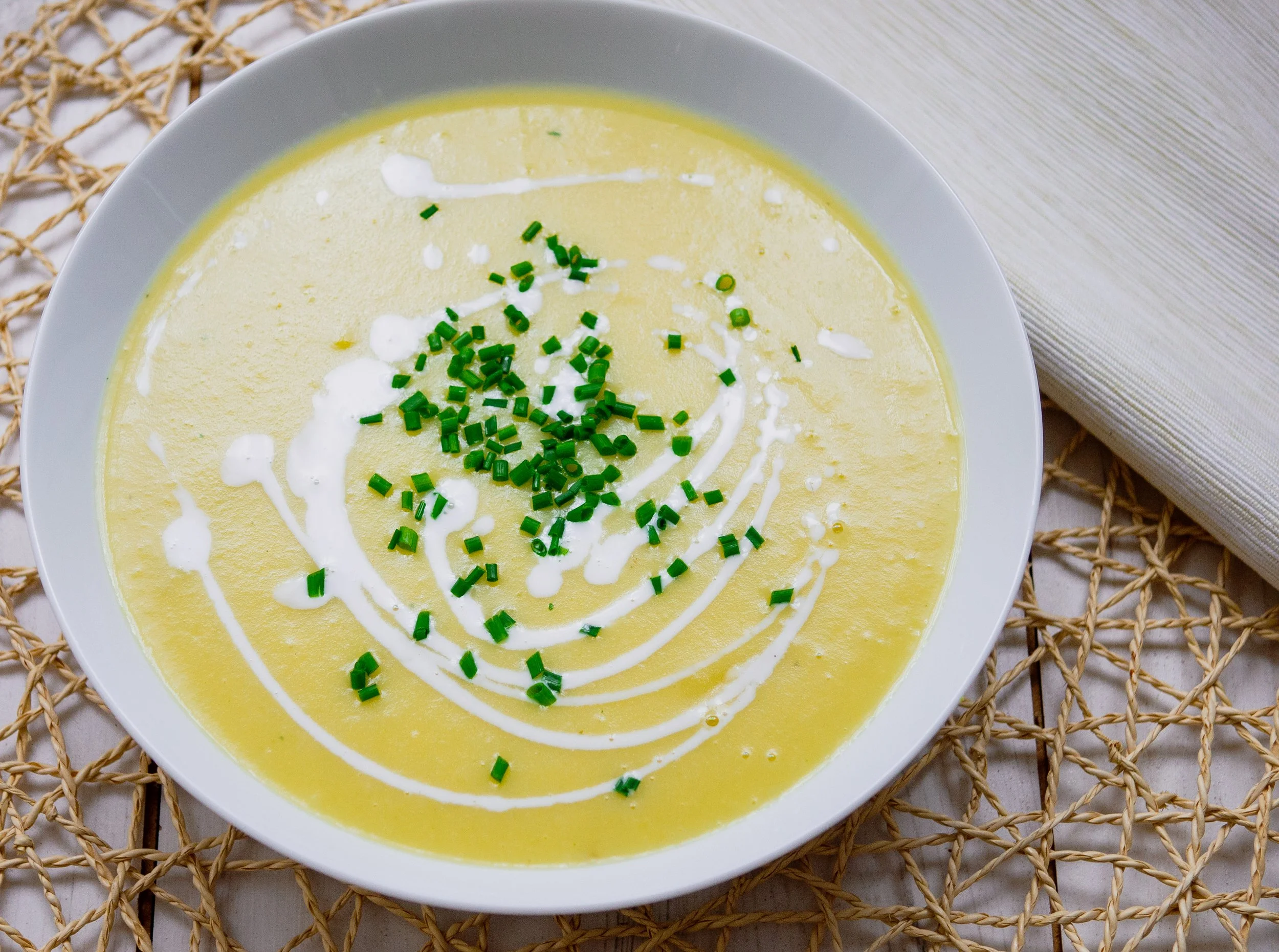 Leek and potato soup  in a white bowl on a table with a cream and wicker place setting
