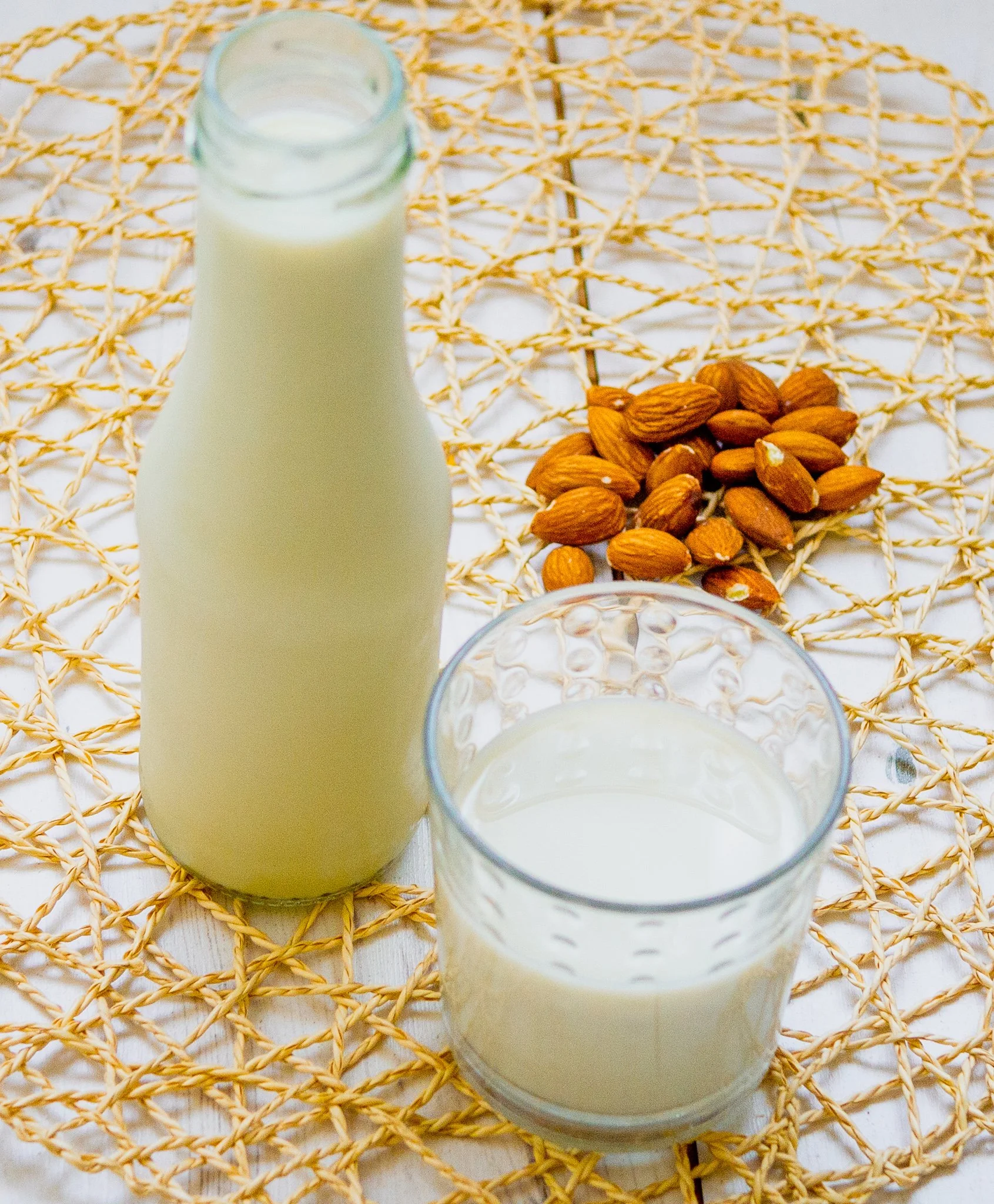 A bottle and a glass with almond milk and a small pile of almonds