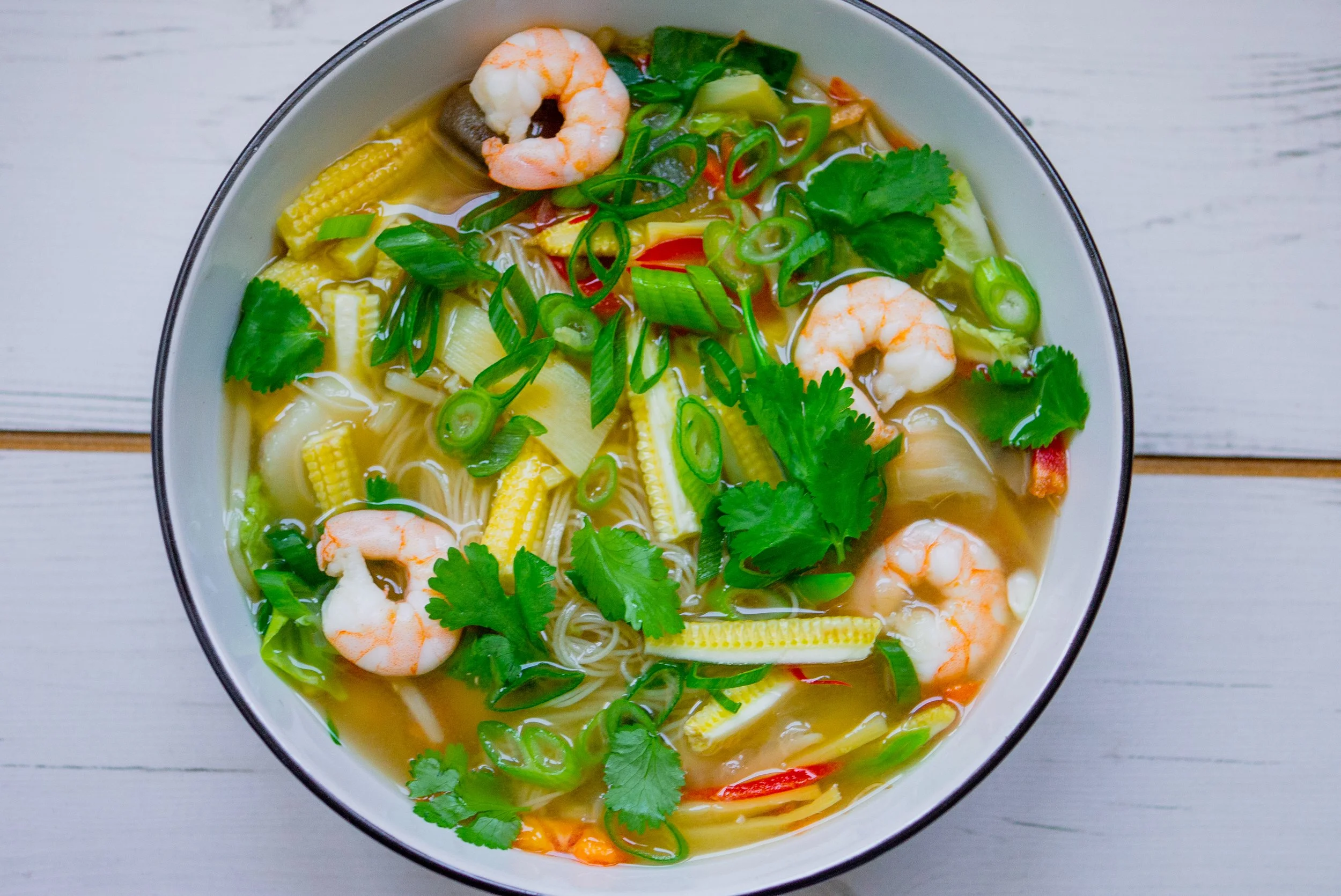 A bowl os Asian style soup with prawns and vegetables in a clear broth