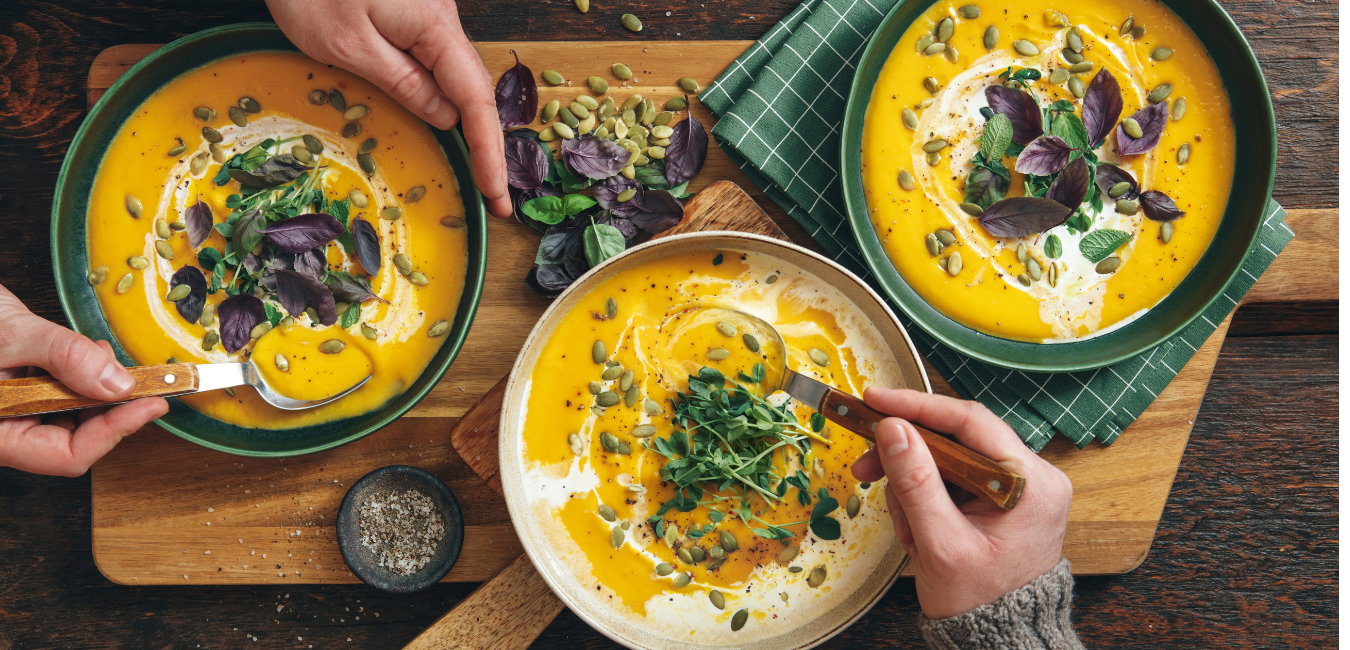Wooden table with 3 bowls of orange coloured soup drizzled with cream and pumpkin seeds
