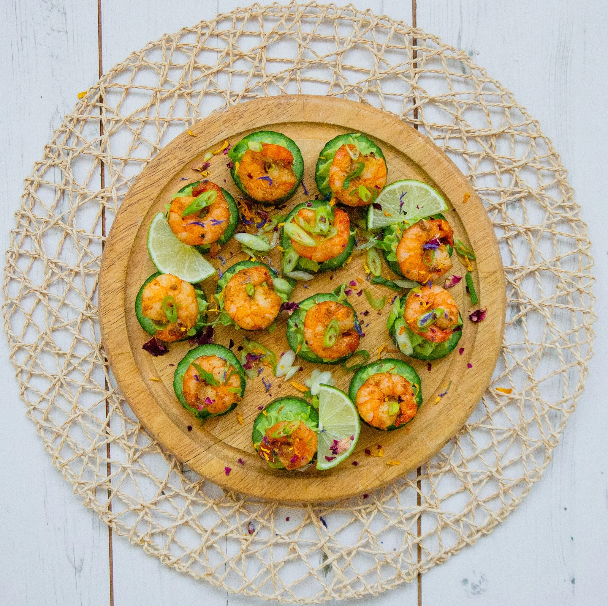 cucumber and prawn canapes with piped avocado decorated with flower petals on a round chopping board