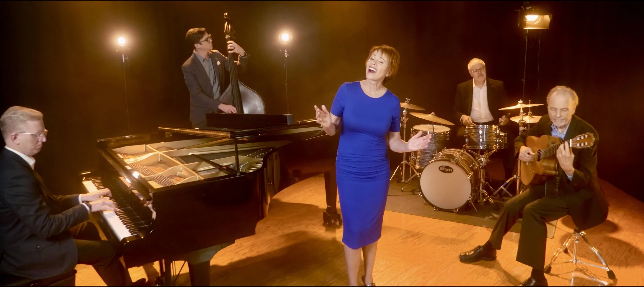 Musician performing with a jazz band in a studio, including a pianist, upright bassist, singer, drummer, and guitarist.
