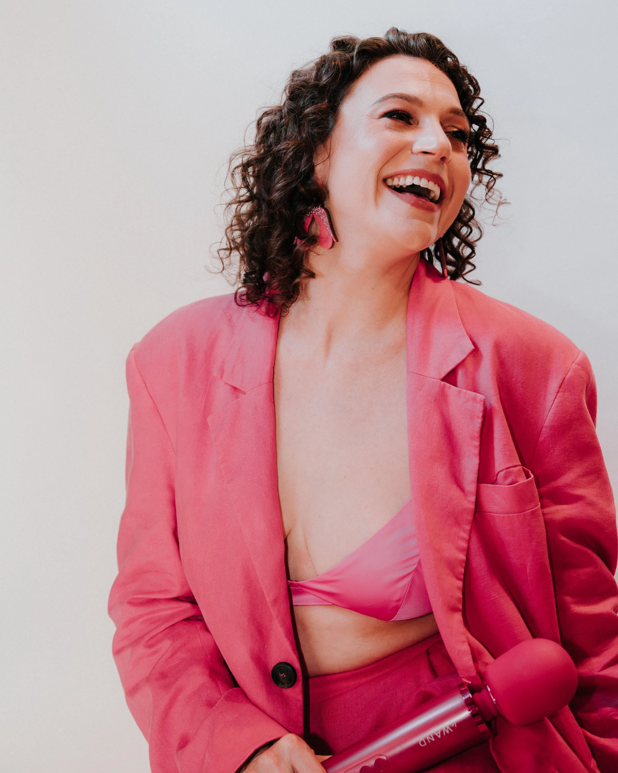 Cady S. Moore, sex educator and coach, laughing in a pink blazer holding a Le Wand massager