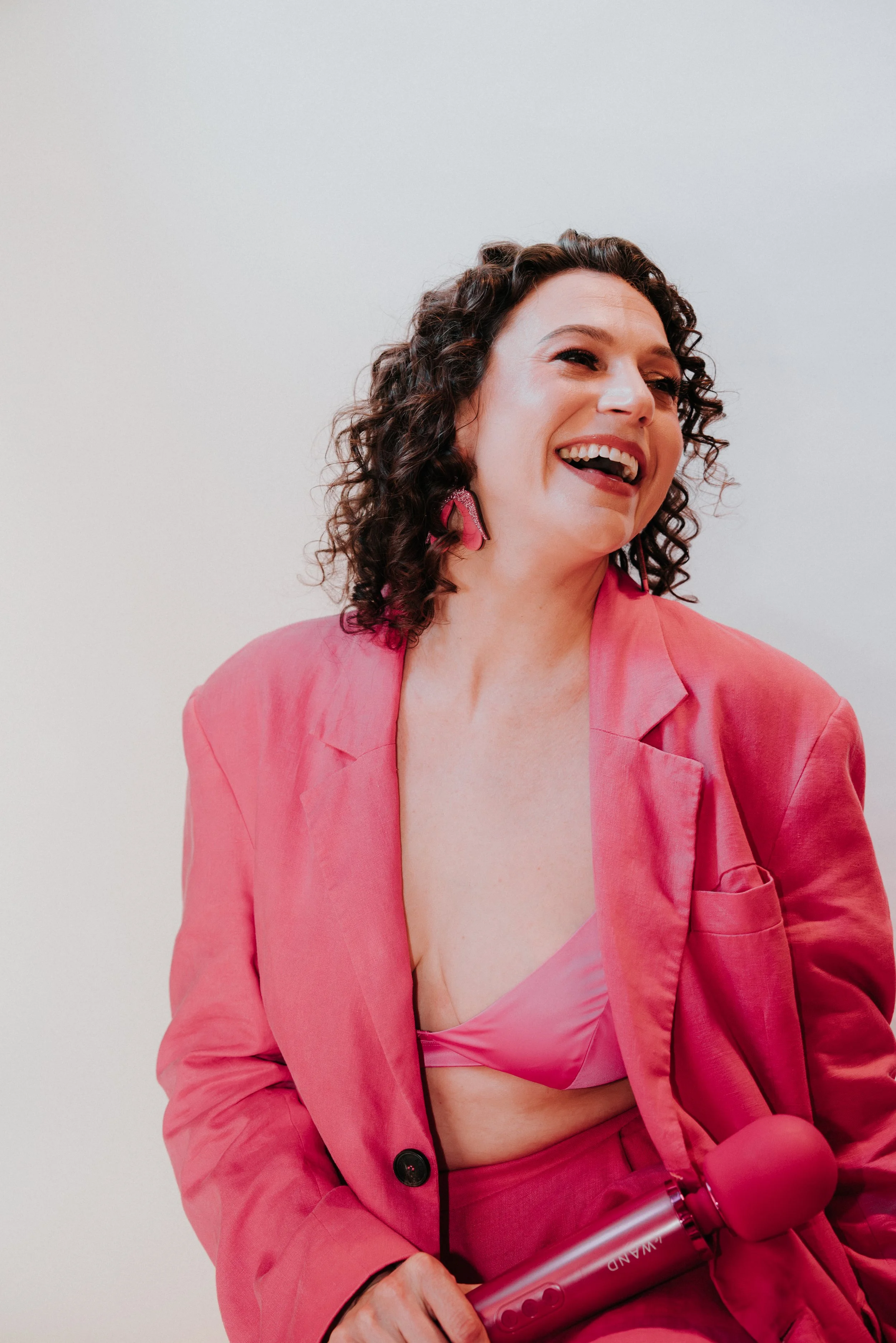 Cady S. Moore, Sacramento sexuality educator and coach, laughing joyfully in an open pink blazer during a professional photo shoot