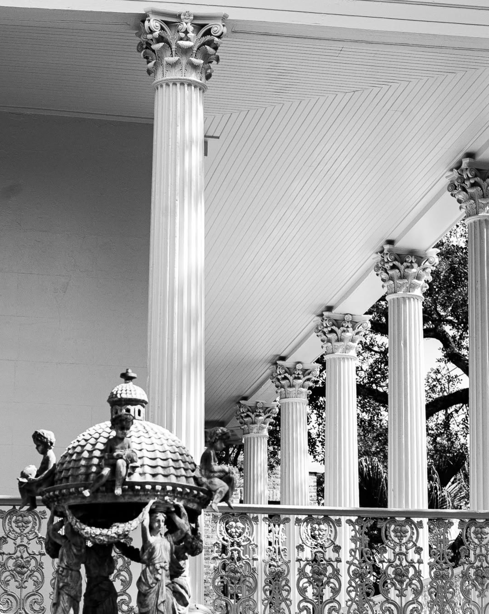 A black and white image of a veranda with classical columns and a detailed iron bannister