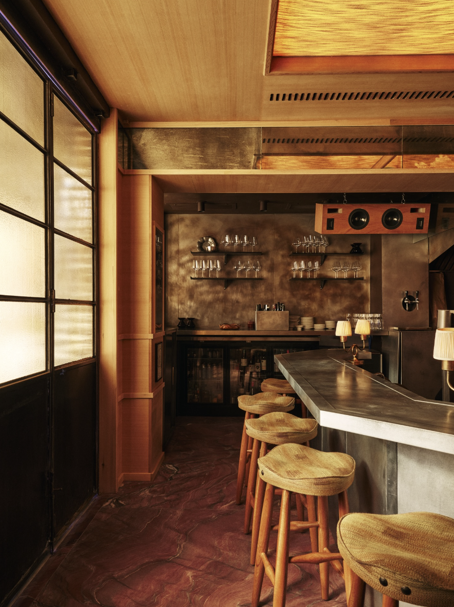 A cozy restaurant interior with a bar and bar stools, with more seating in the rear and wine bottles and glasses on shelves