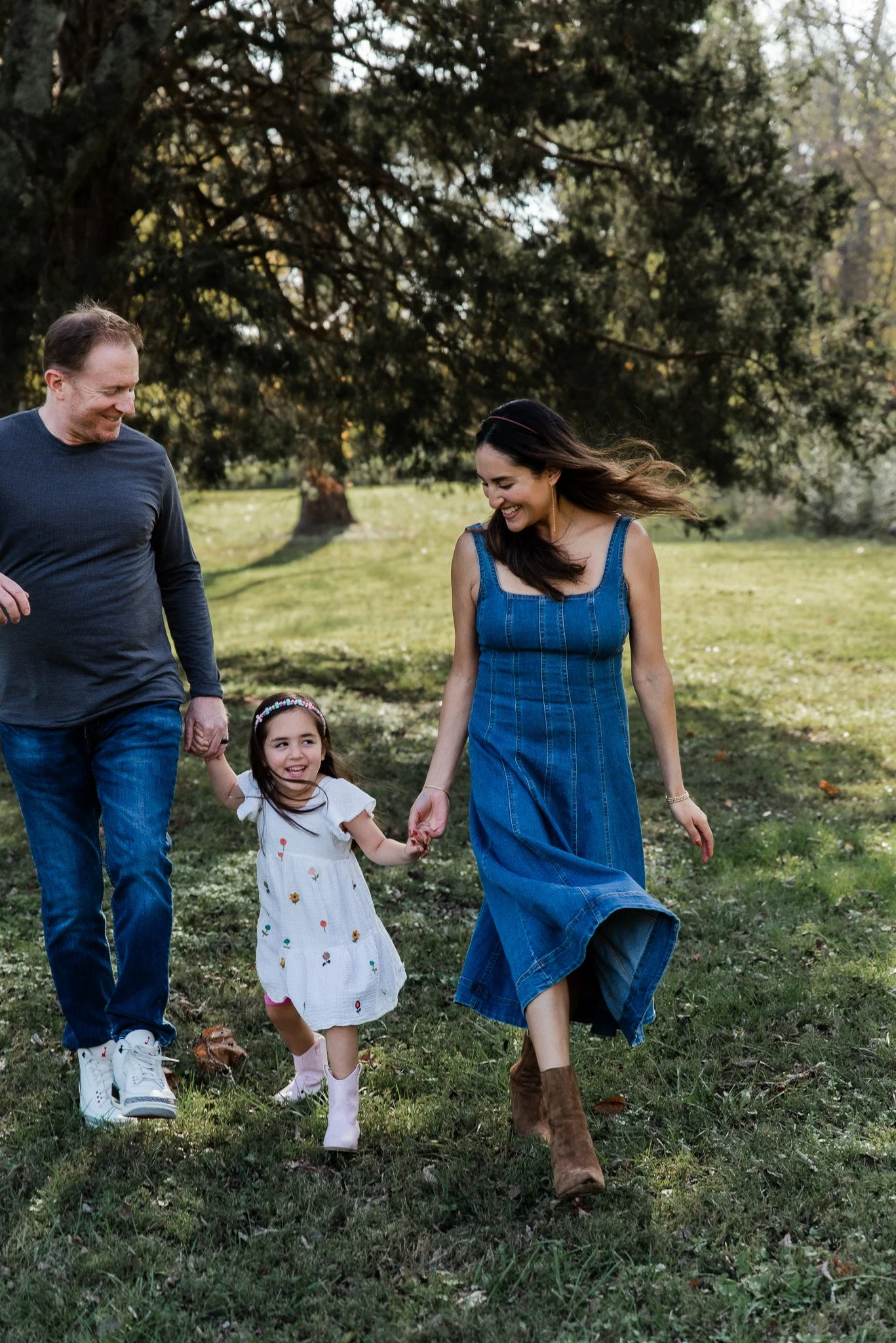 A little girl is walking in the middle of her parents while holding both their hands.