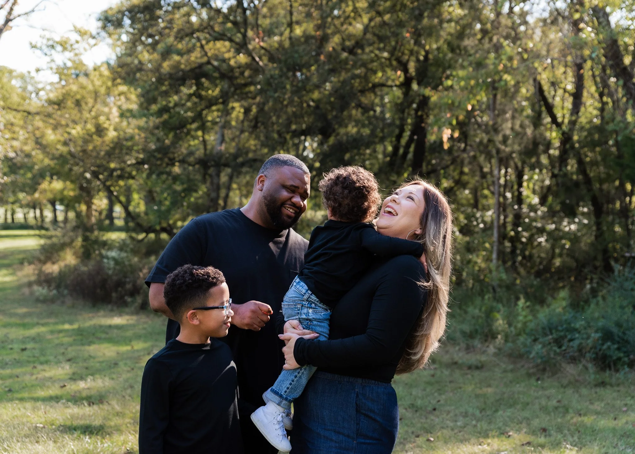 A mom laughs while holding her small child. Her husband and other child smile as they look on.