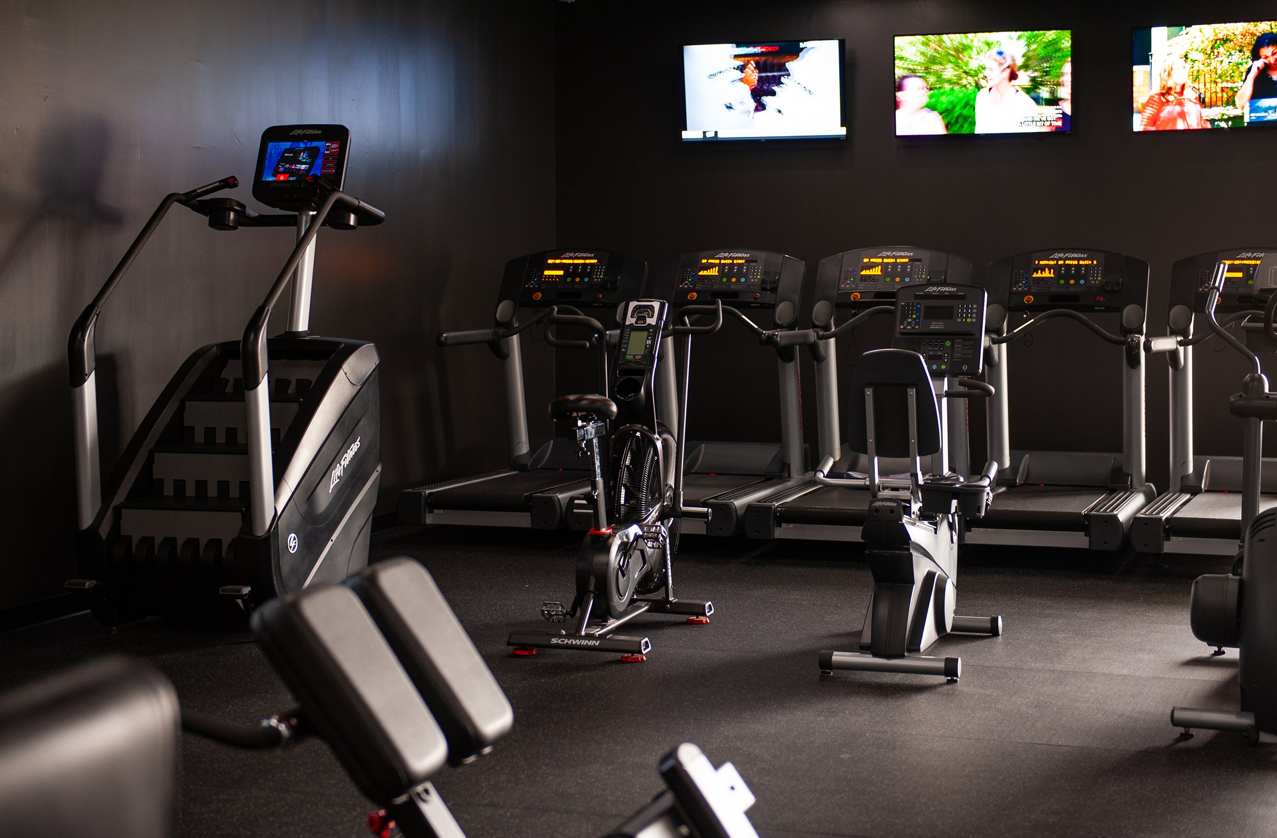 Gym with treadmills, stair machine, exercise bikes, and wall-mounted TVs.
