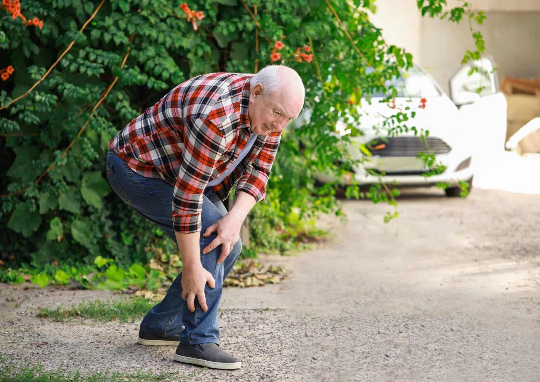 Older man bending forward and holding his leg in pain while walking outdoors