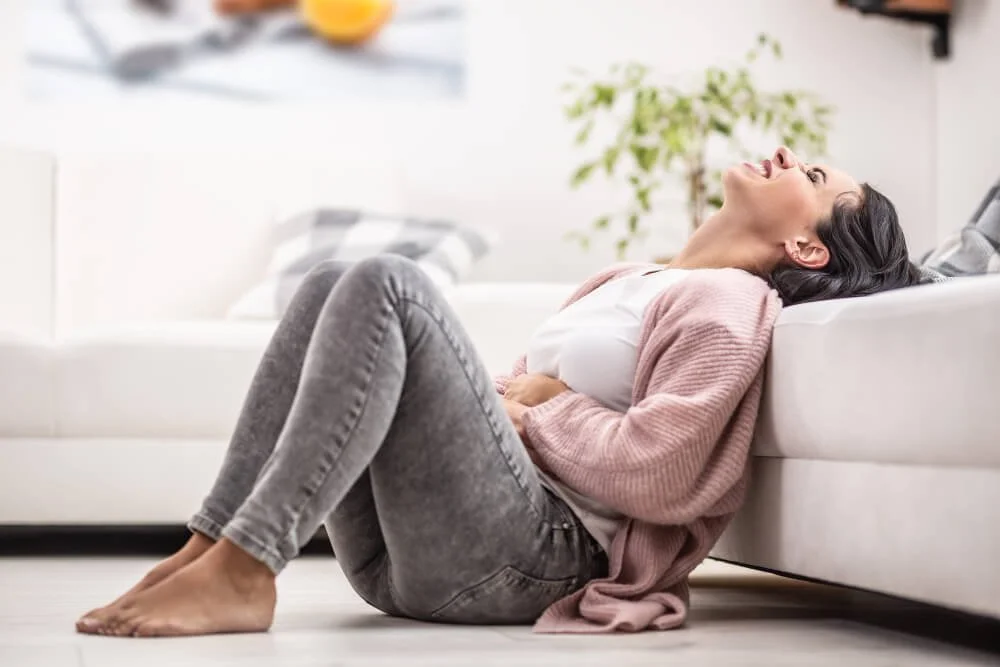 Woman lying on a couch holding her lower abdomen in pain from chronic pelvic pain