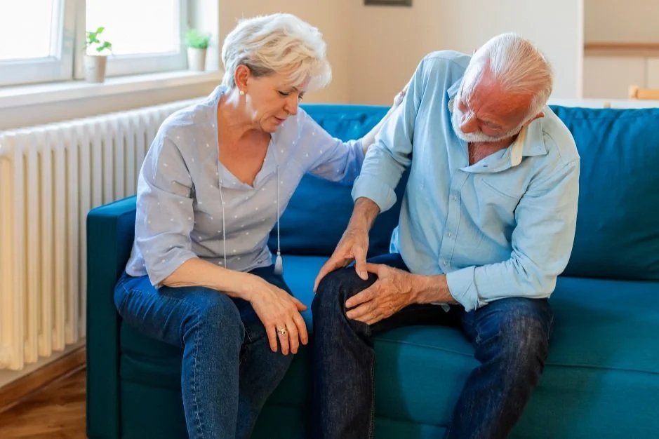 Older man holding his painful knee while his wife comforts him