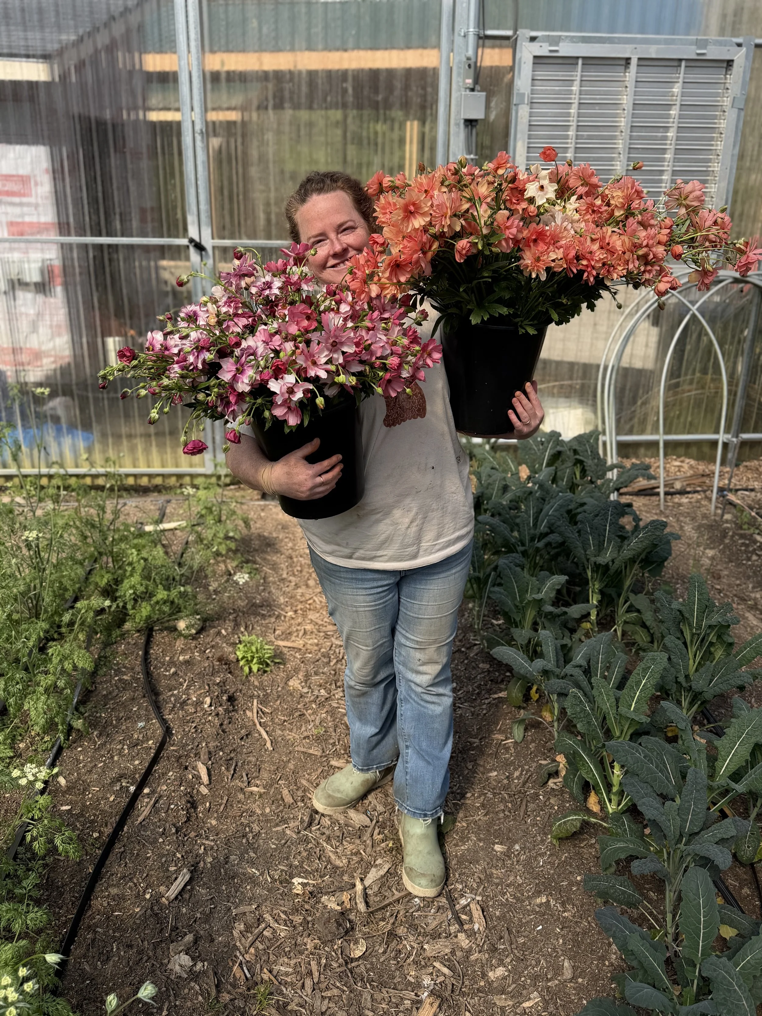 Jodi Logue holds a bucket of brightly colored flowers in each arm and smiles