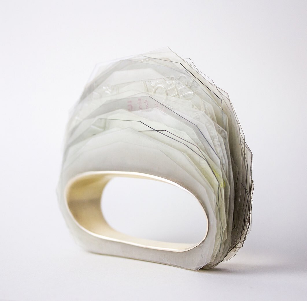 Here is a bit of a throwback to one of the last pieces I made in school. It is a bunch of layers of cut plastic from salad/berry/to-go containers held together by a ring of silver. 

It reminded me of holding a small mountain range in my hands when w
