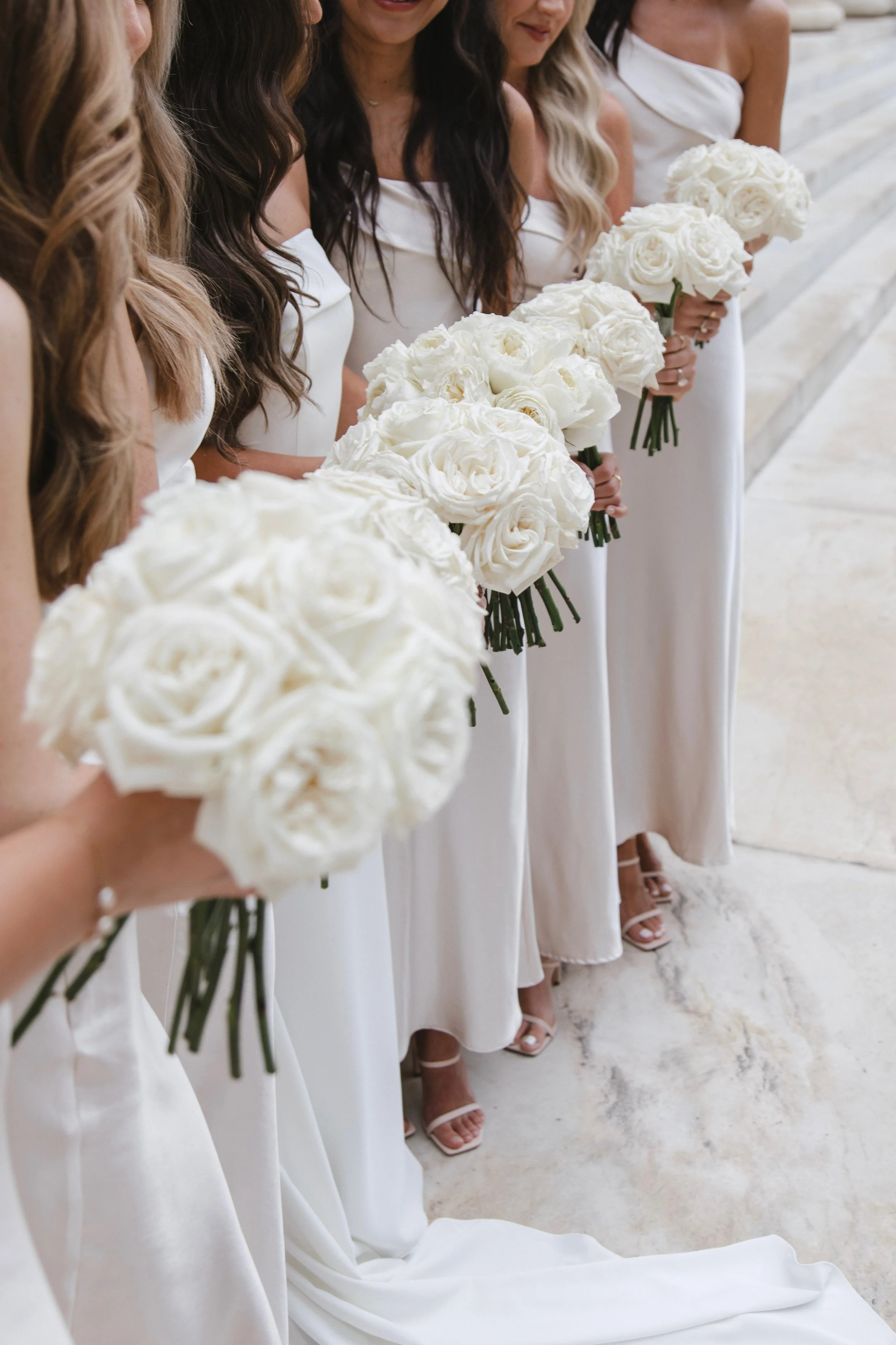 Bridesmaids in white dresses holding white bouquets at a wedding ceremony.