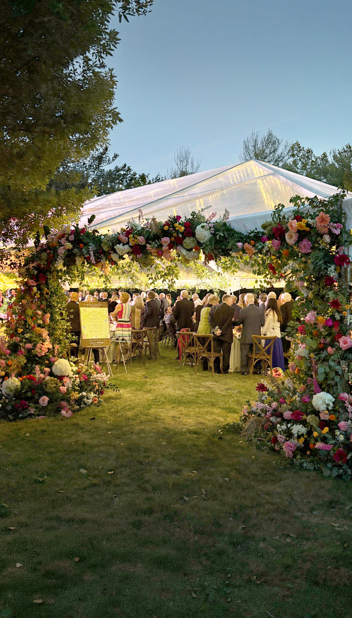 An outdoor wedding reception under a large tent decorated with colorful flowers.