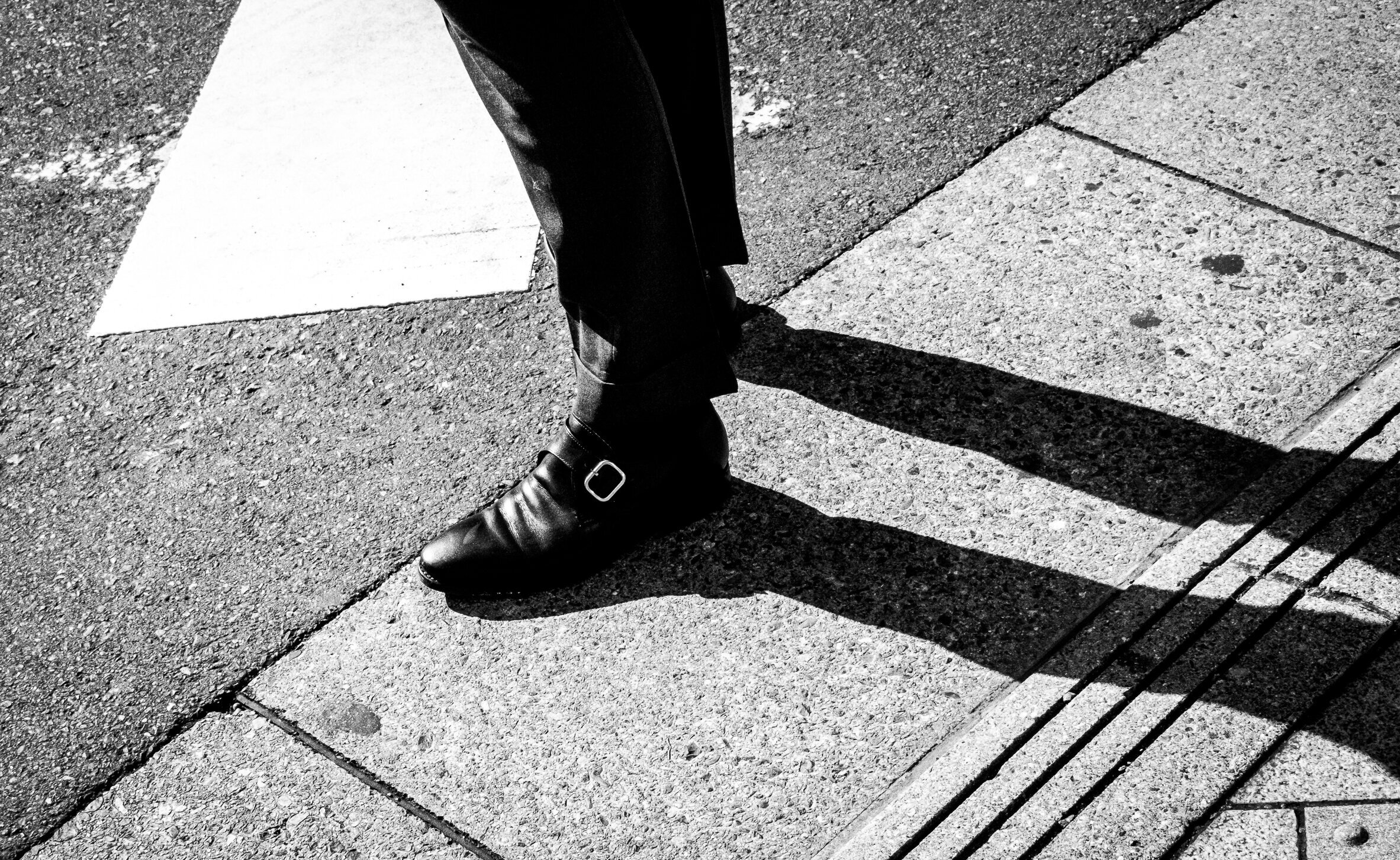 Sabates masculines amb ombra al carrer, en blanc i negre.