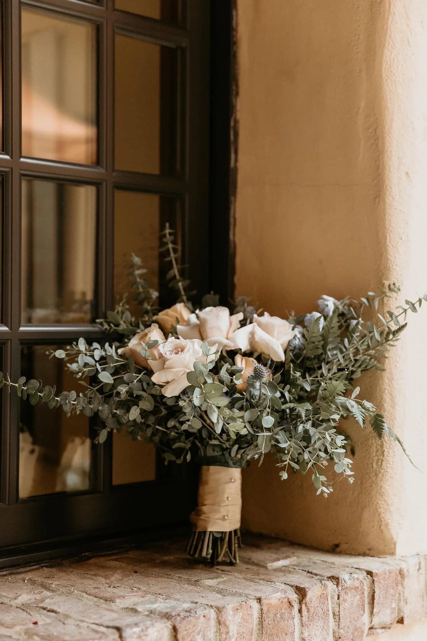 Bouquet of white roses and greenery on a brick ledge next to a window.