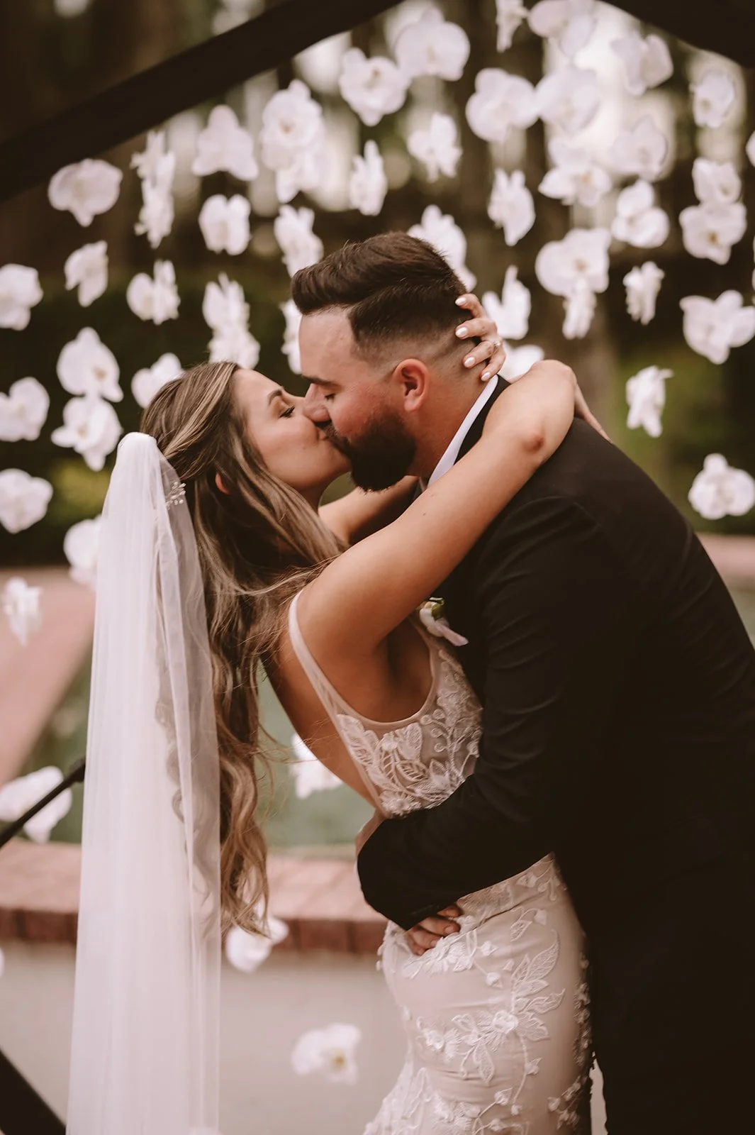 Bride and groom kissing in front of floral arch on their wedding day.