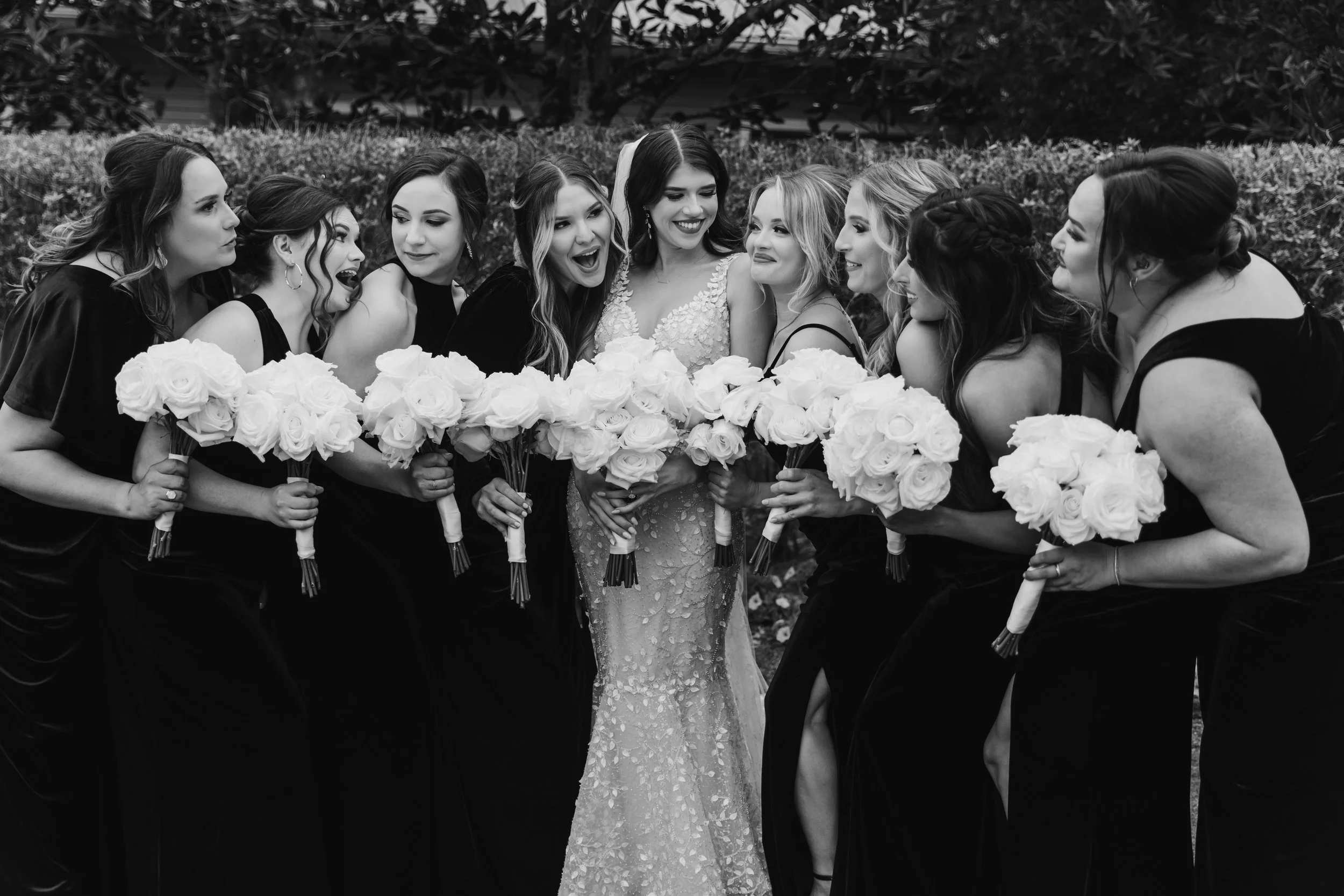 Bride and bridesmaids posing with bouquets, wearing formal dresses, in a celebratory and joyful manner outdoors.