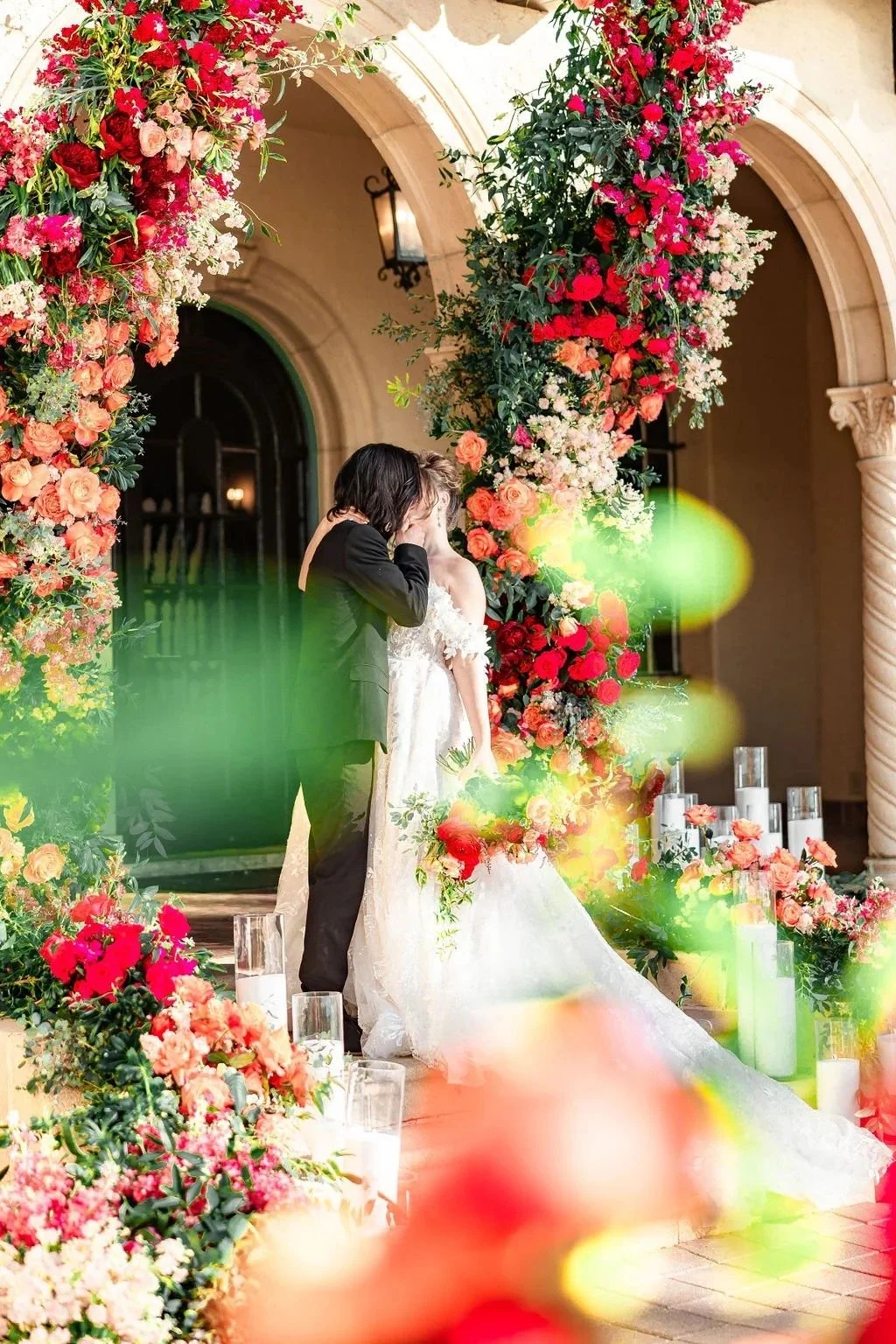 bride and groom kissing underneath lush floral arches of red and orange, created by Orlando wedding florist JF Events & Flowers
