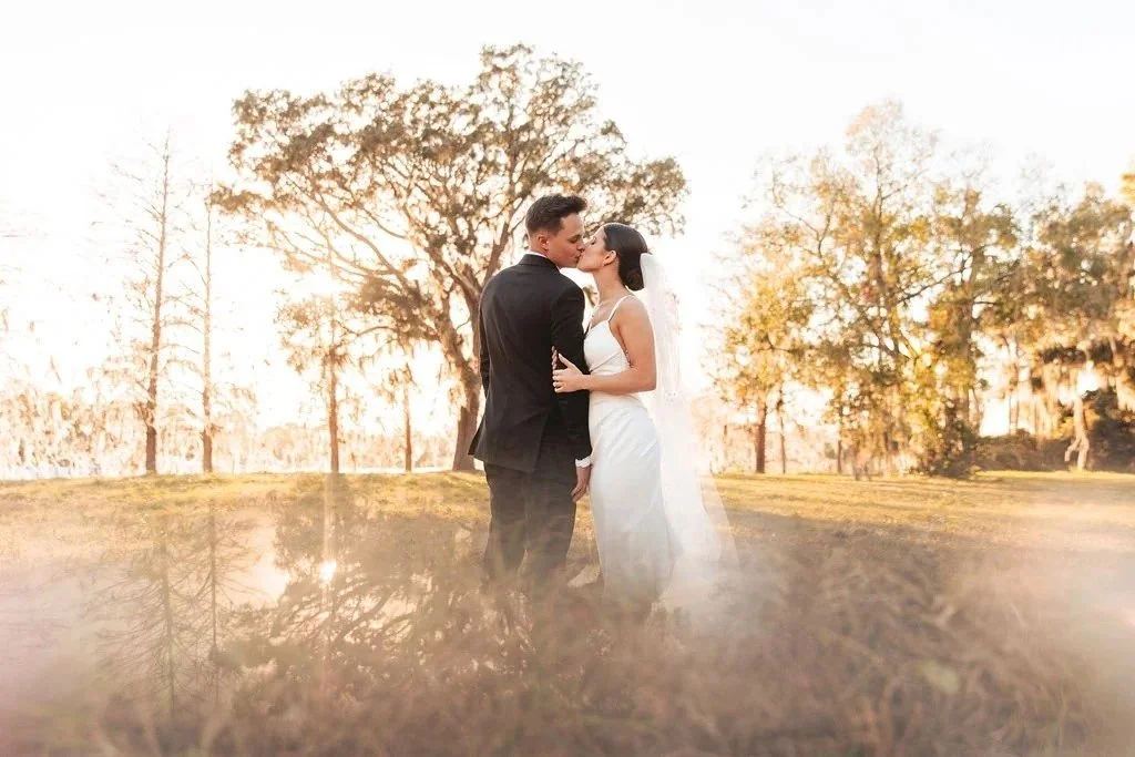 Orlando bride and groom kissing outdoors with trees in the background, wearing wedding attire.