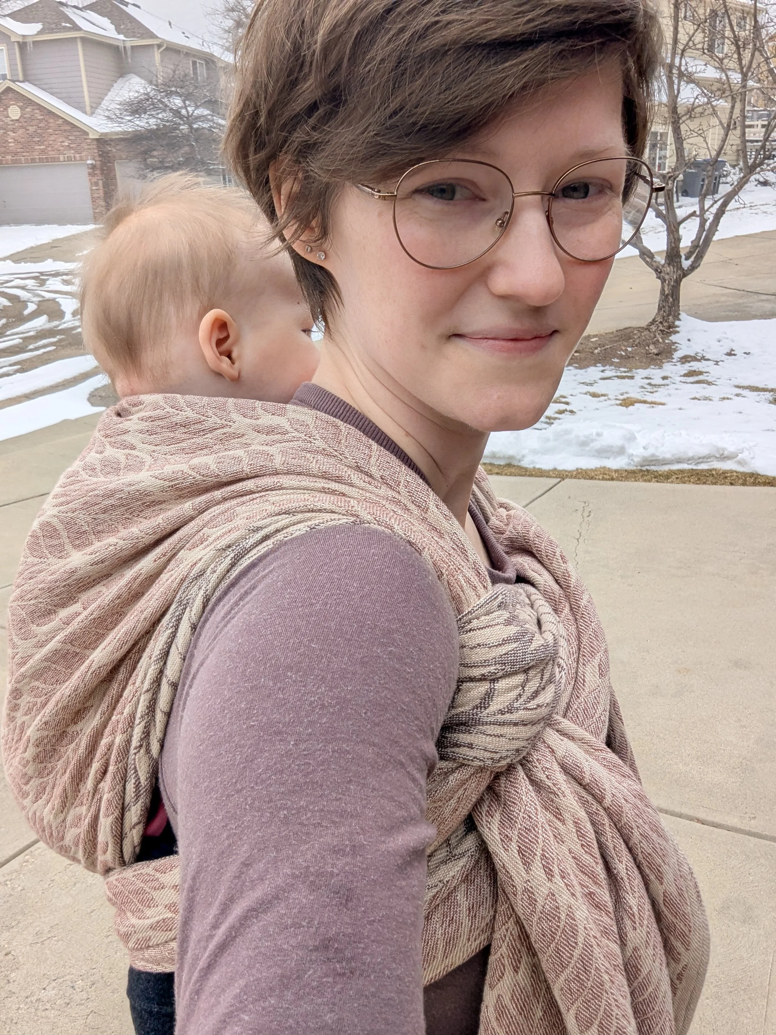 White woman with short blonde hair with a baby wrapped on her back with a beige woven wrap