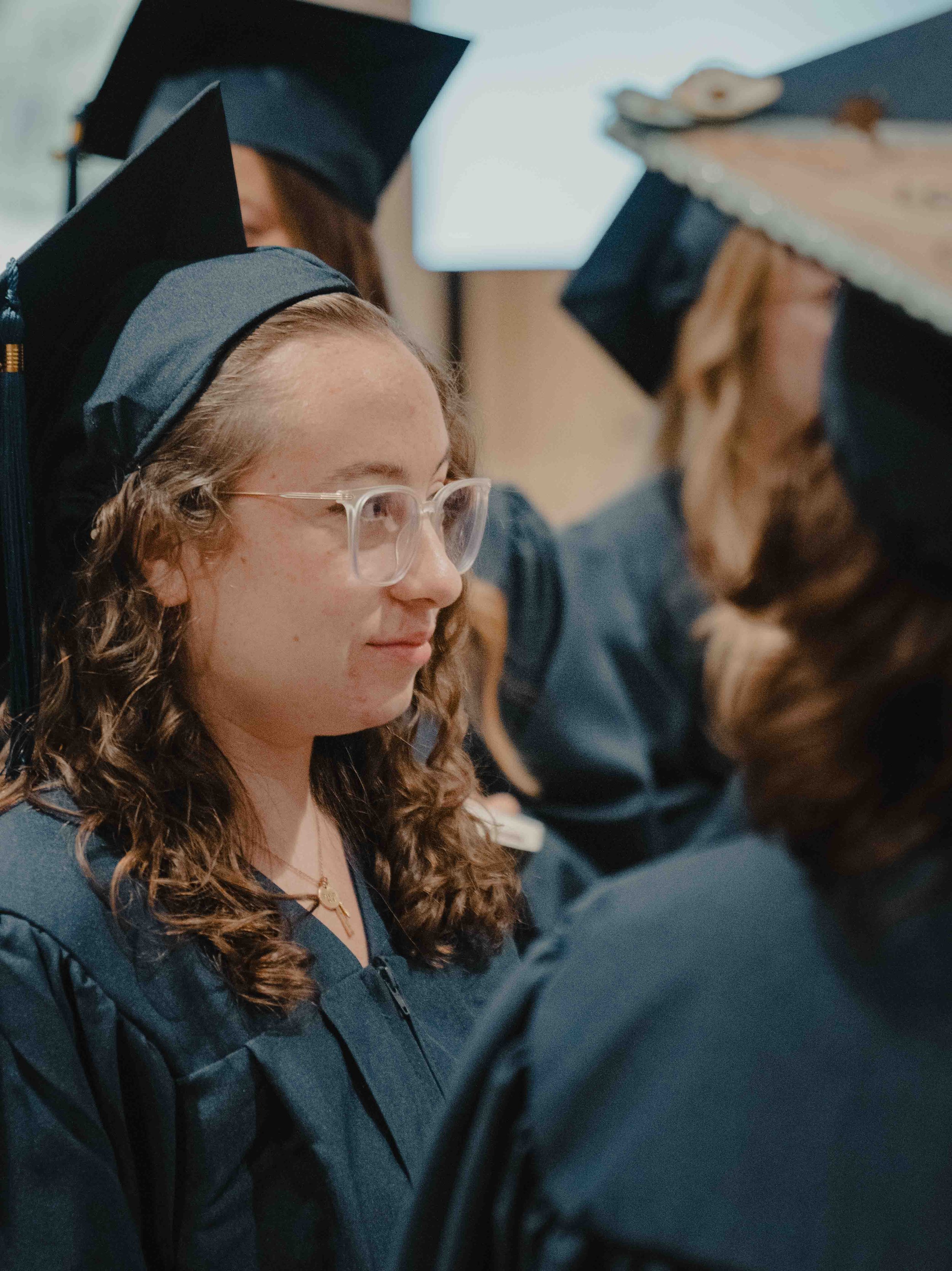 A group of graduates in blue caps and gowns standing in a line, heads bowed for a graduation ceremony.