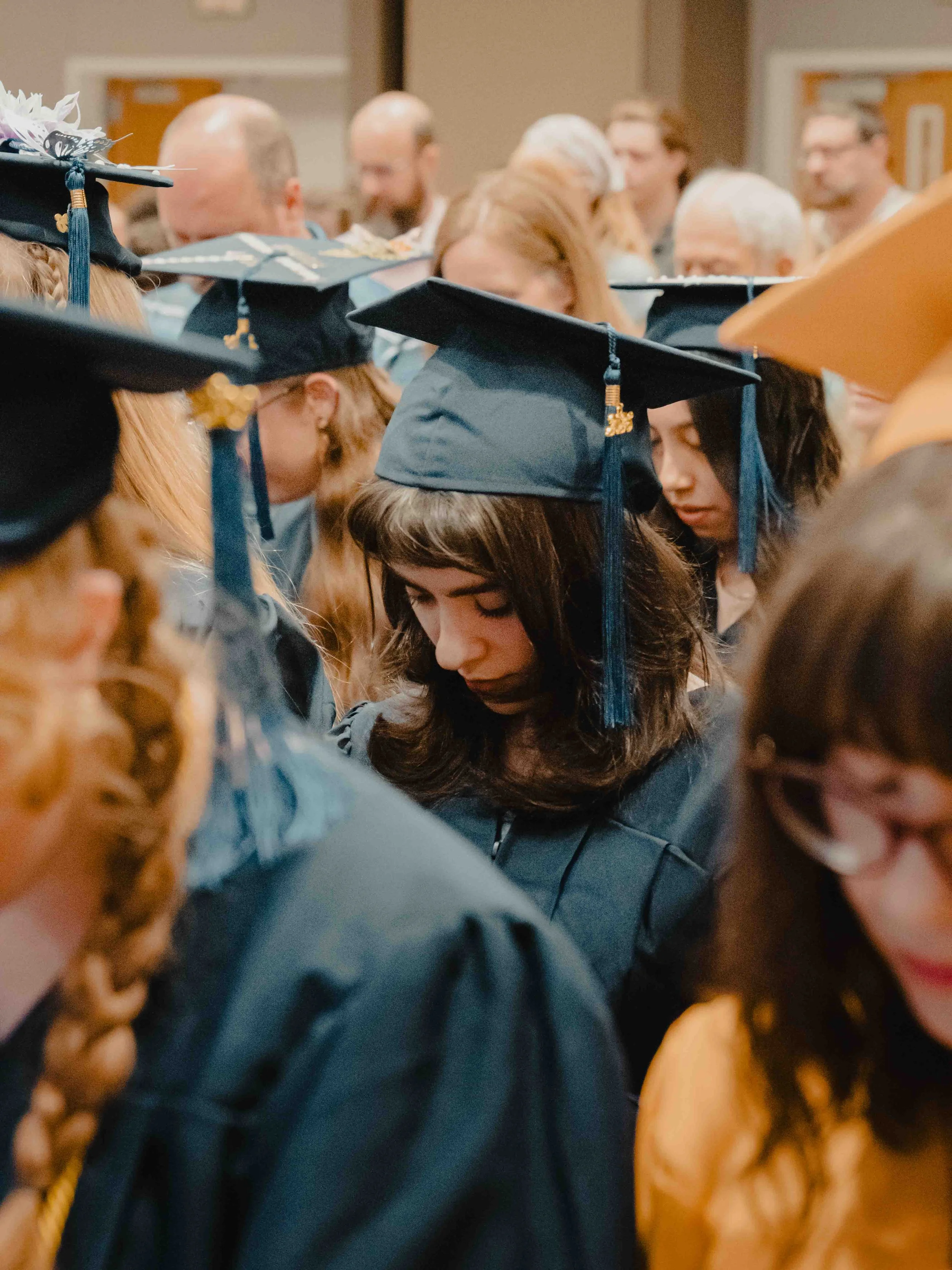 People attending a graduation ceremony, wearing traditional caps and gowns, with some focusing prayer or reflection.
