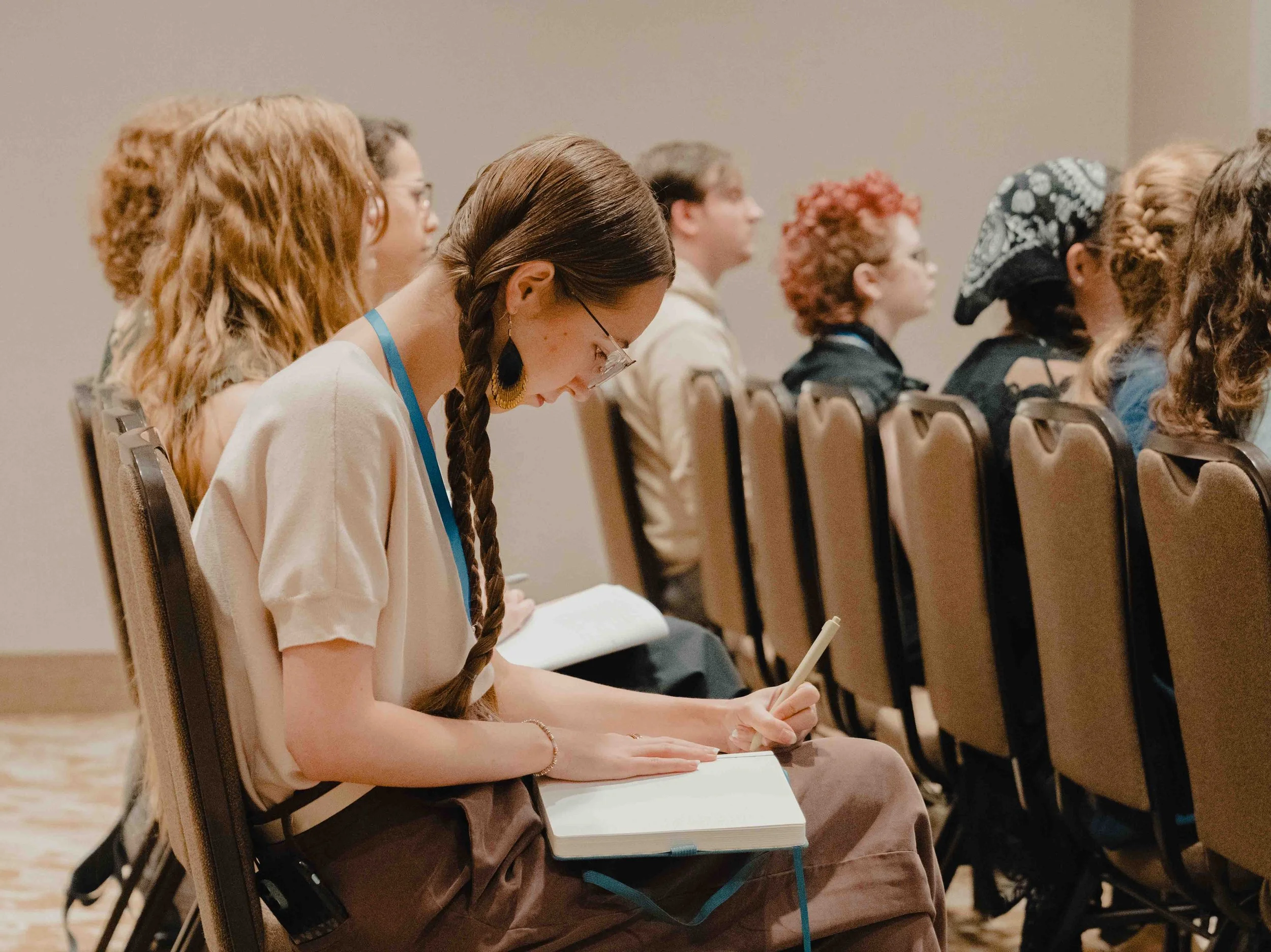 A group of diverse people seated in a conference room, attentively listening and taking notes.