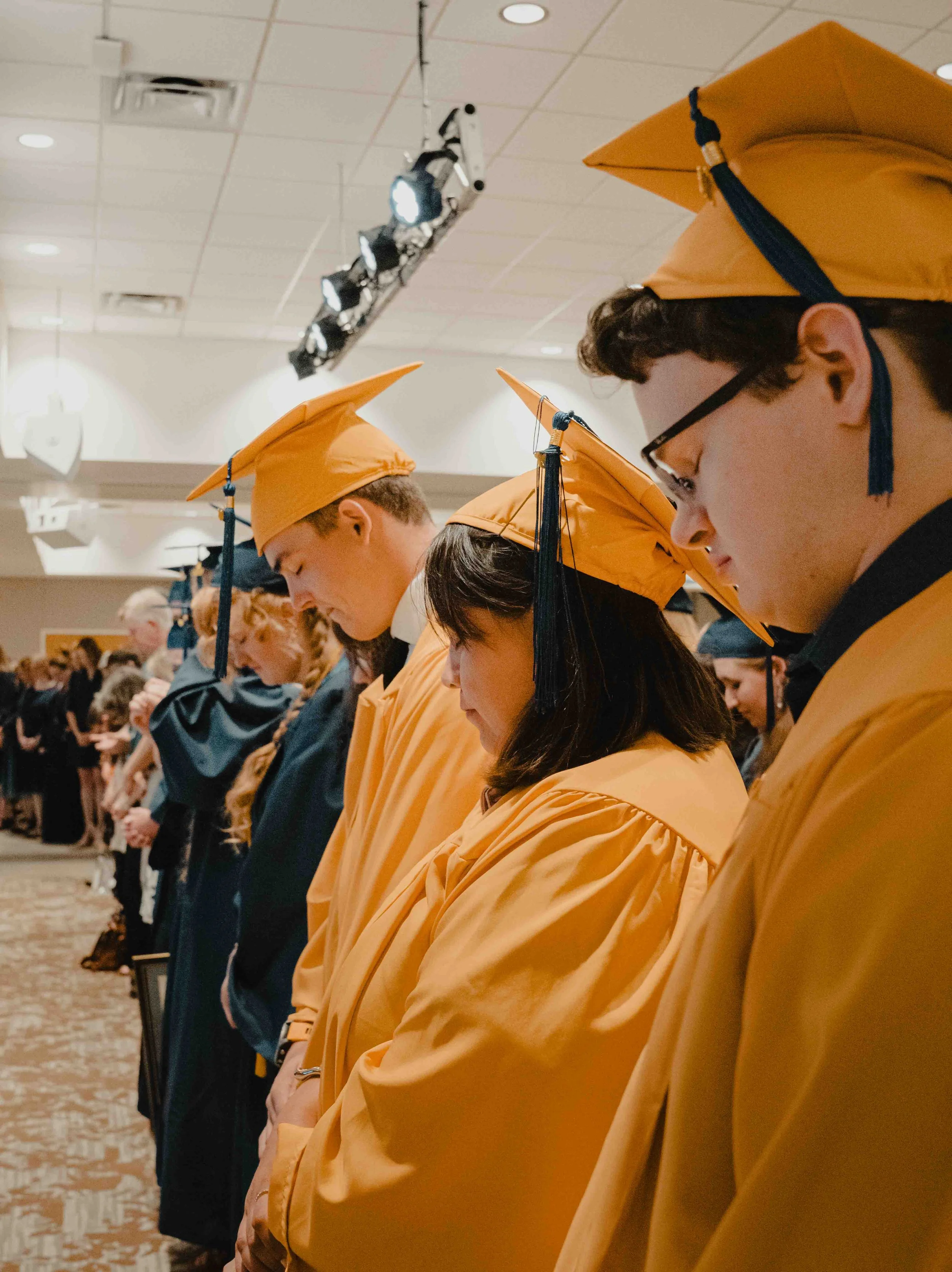 Line of graduates wearing yellow caps and gowns standing during a ceremony.
