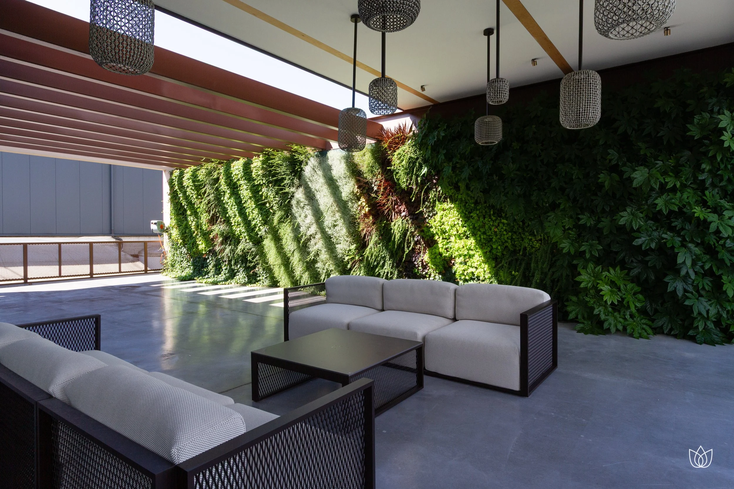 Lounge area with white chairs and sofas with black frames, black table, ceiling with designer lamps, and a green wall with plants in a modern and bright setting.