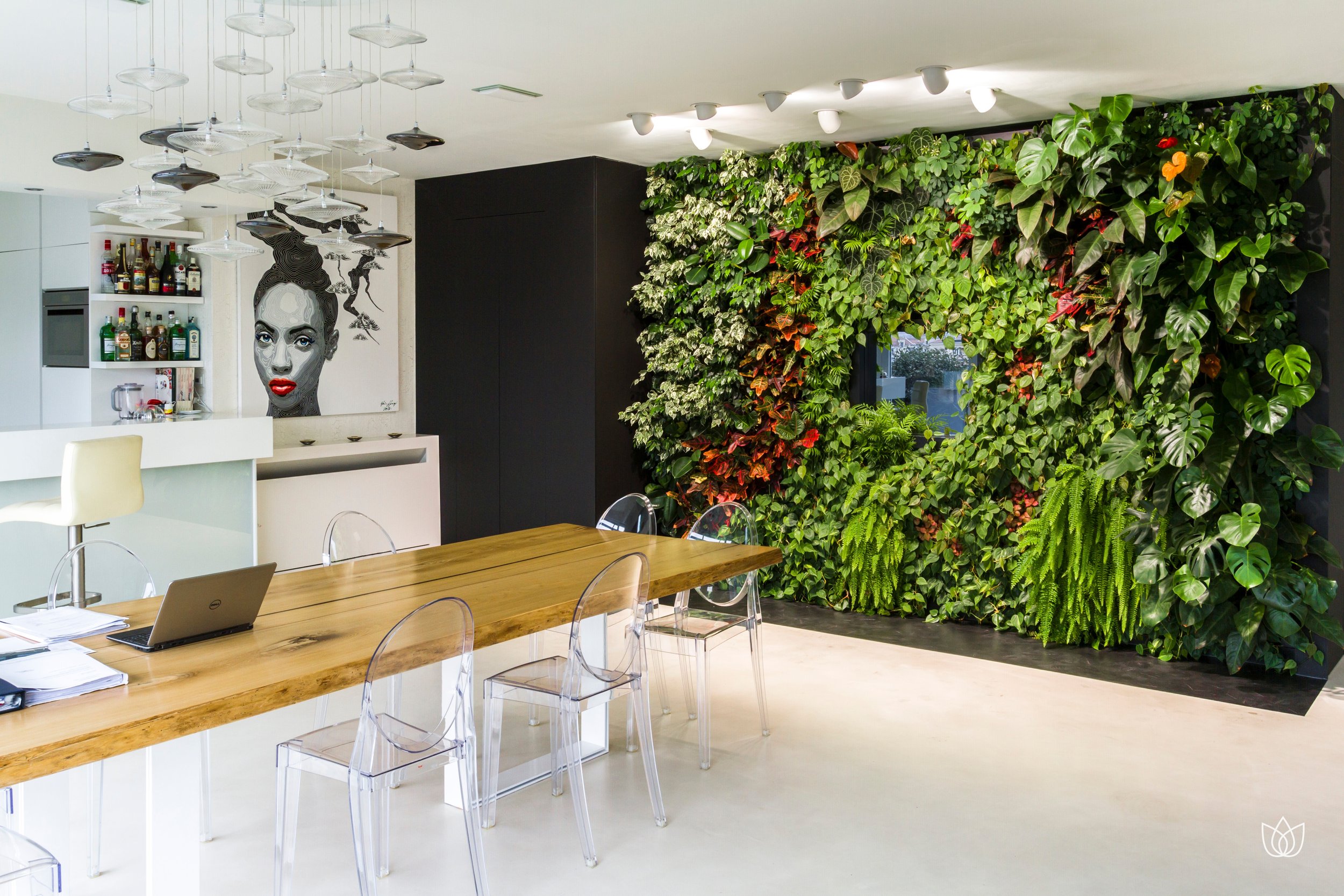 Meeting room with vertical green wall, wooden table, transparent chairs, white walls and modern chandelier