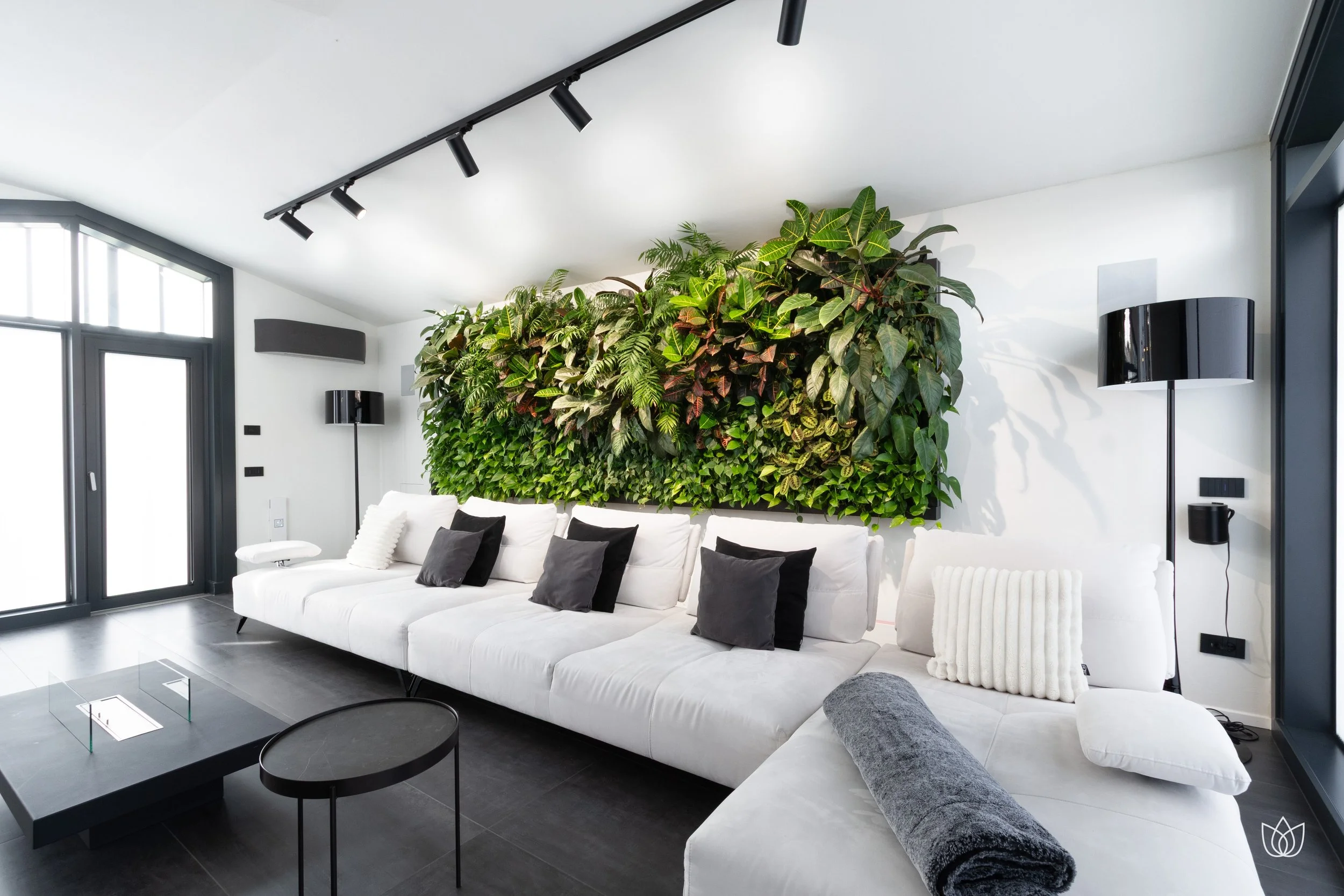 Modern living room with white sofa, black cushions, and green wall pattern with plants