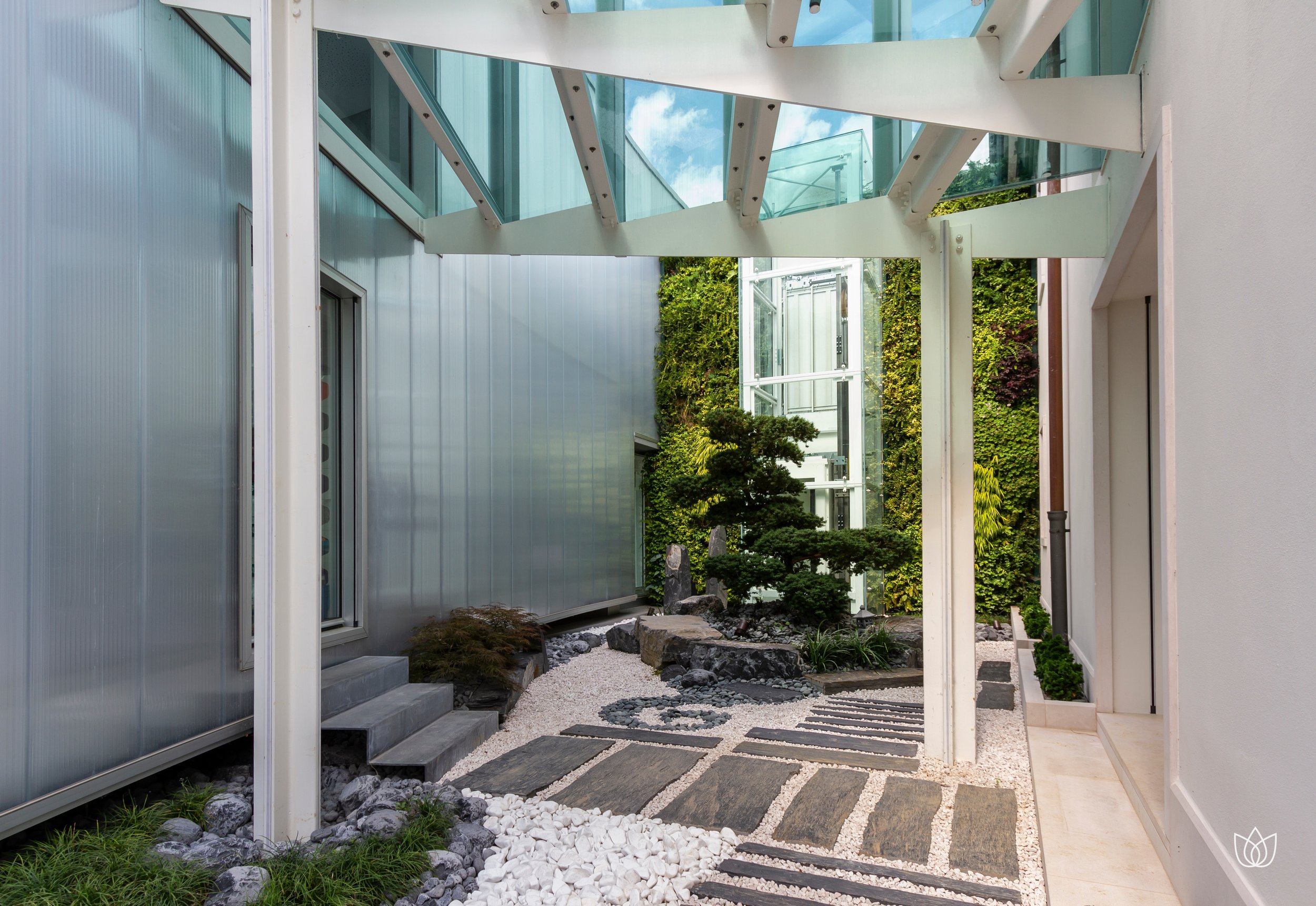 Zen garden with bonsai trees, decorative stones and pebble paving, between modern walls and a glass and metal structure