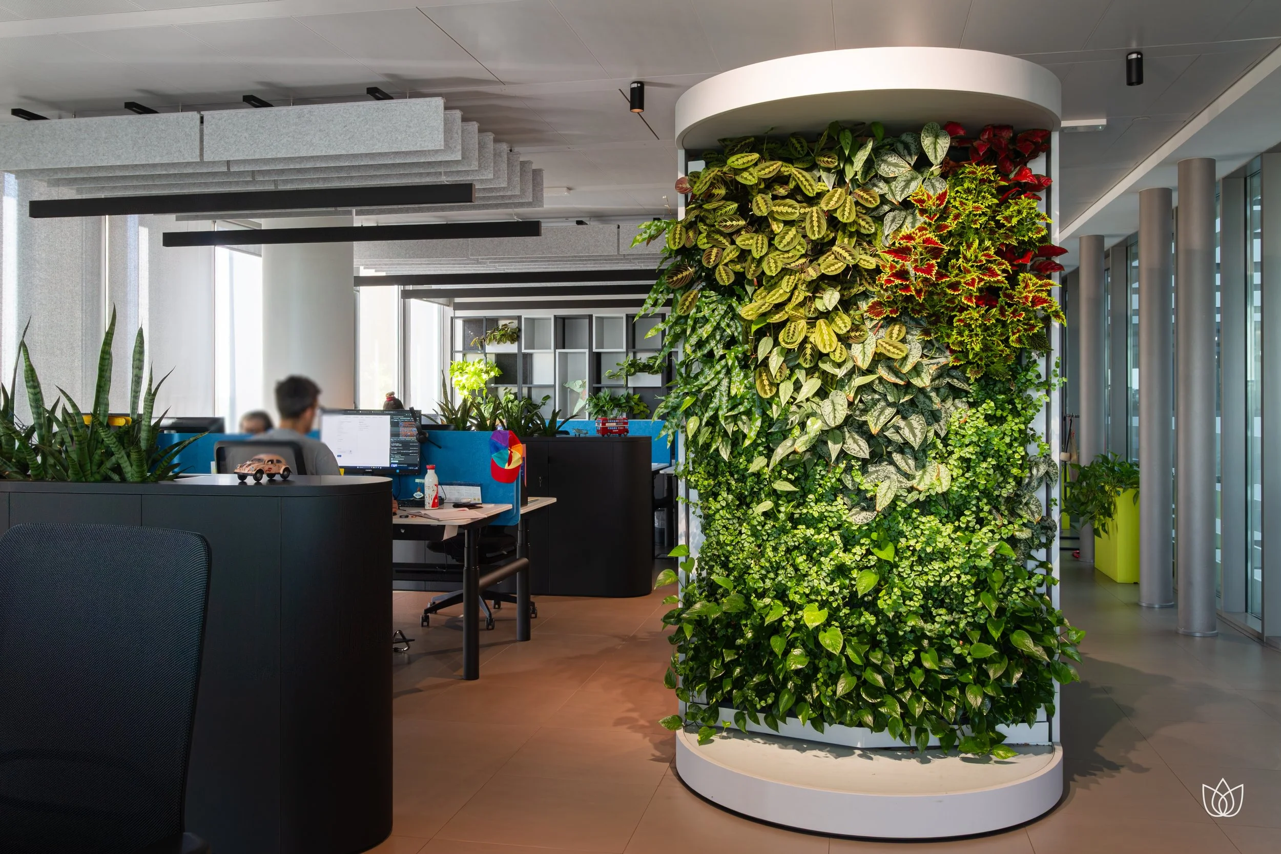 Interno di un ufficio moderno con una parete verde verticale e postazioni di lavoro con schermi. Ci sono piante e arredamento contemporaneo.