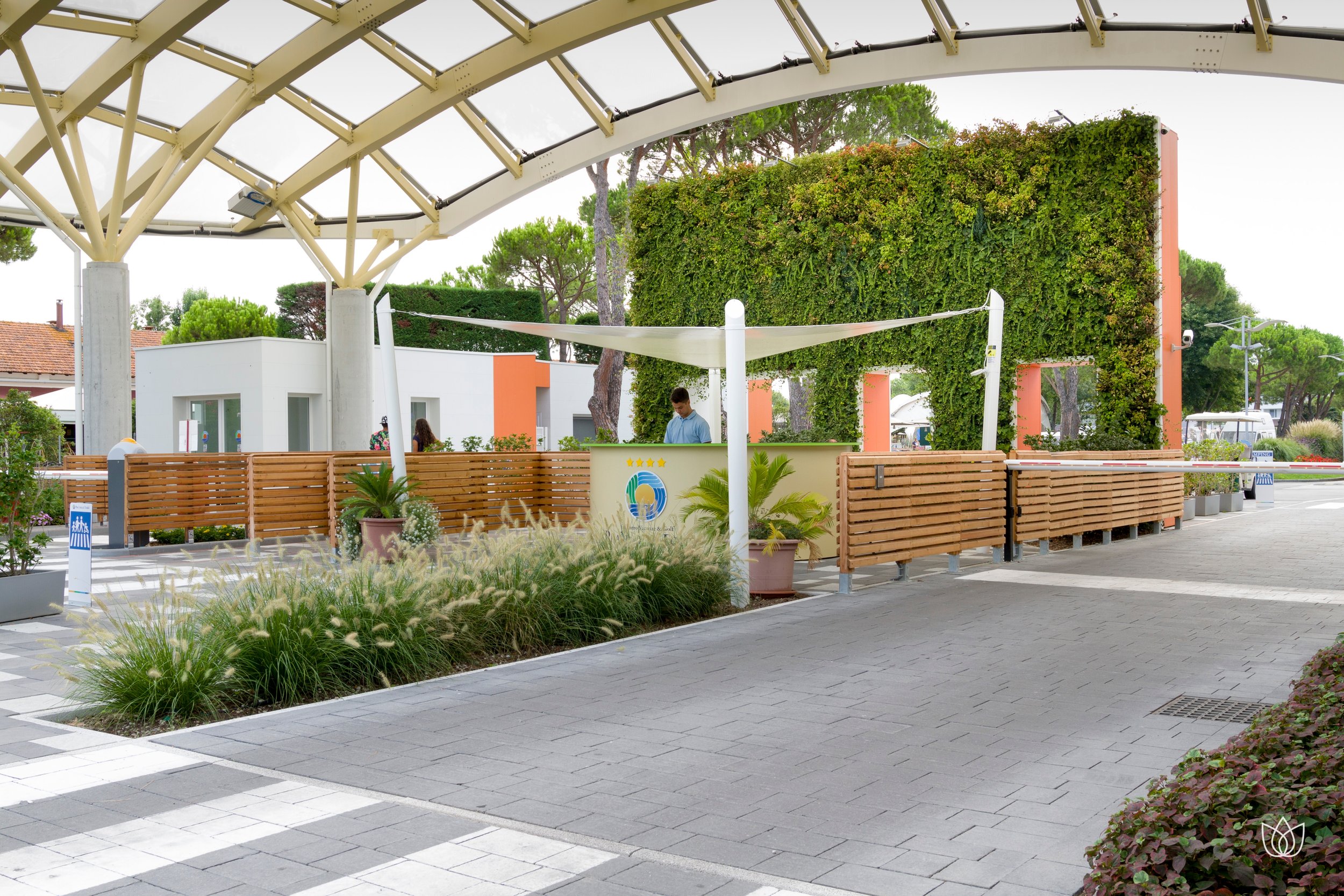 Entrance of a tourist center or reception with personnel, plants and modern facilities, waiting area with wooden chairs and well-kept green environment.