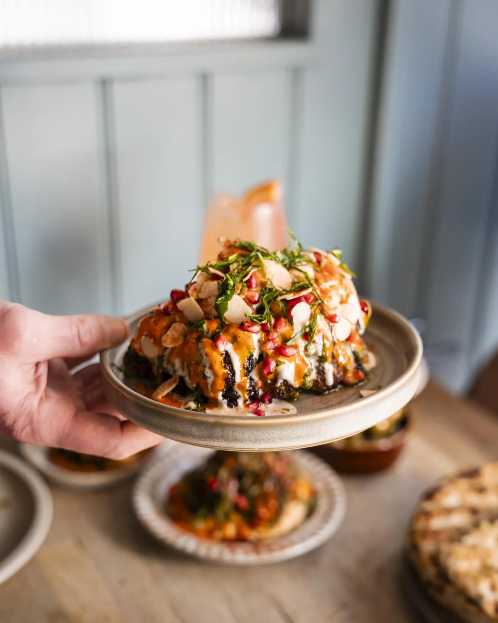 Slice of pumpkin pie on a plate topped with chocolate sauce, crushed pistachios, white sprinkles, and pink flower petals, served on a bed of whipped cream.