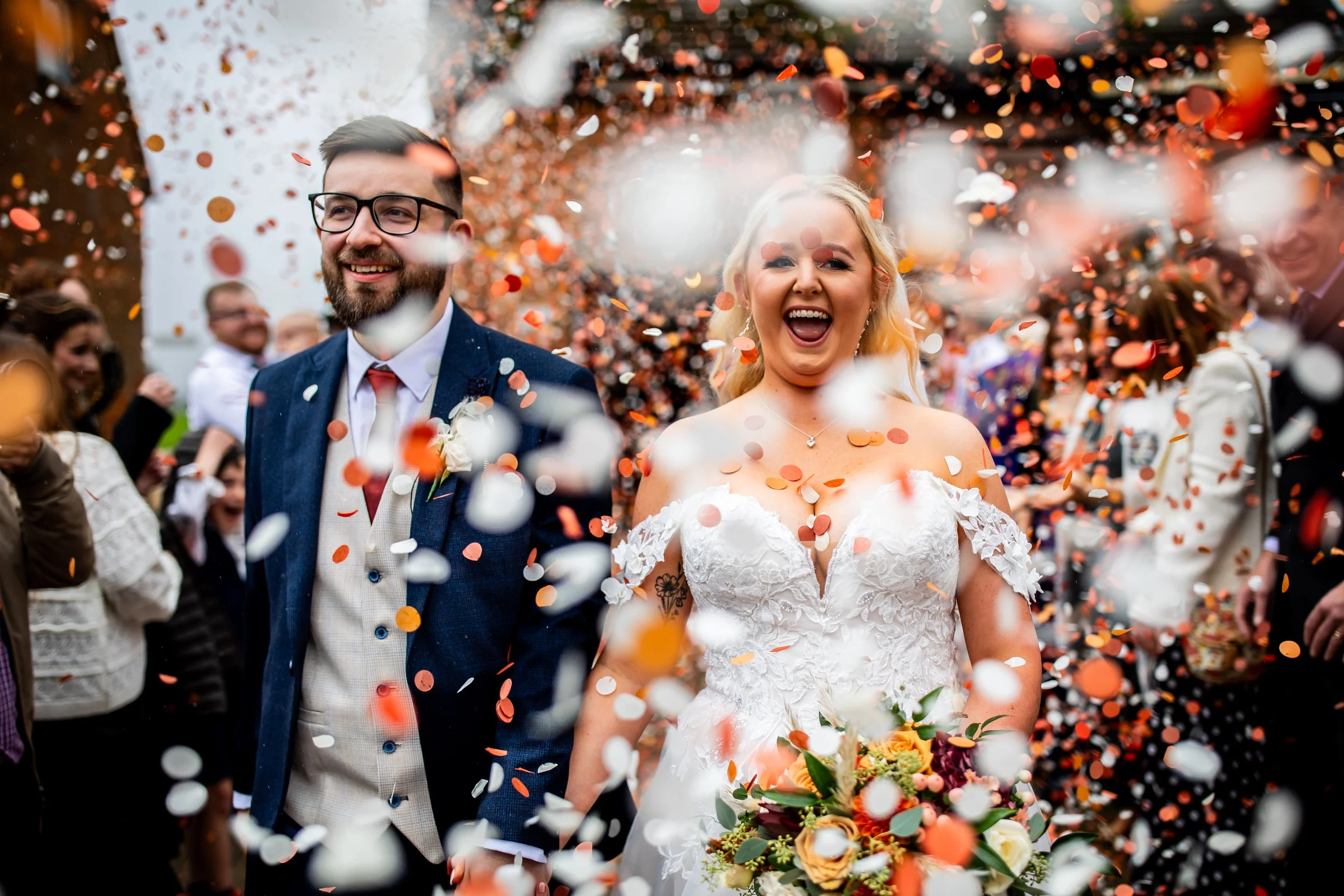 a bride and groom are walking and smiling and laughing through a cloud of lots of confetti towards the camera
