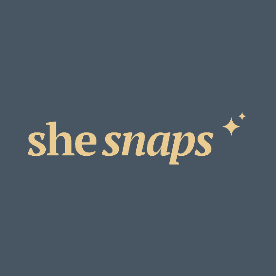 Logo with the text 'she snaps' in beige font on a dark blue background, with two small star icons.
